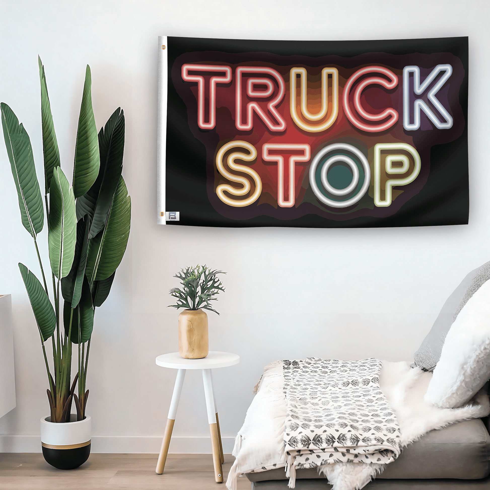 In a home setting, a flag with the saying "Truck Stop" is mounted on a white wall by a side table.