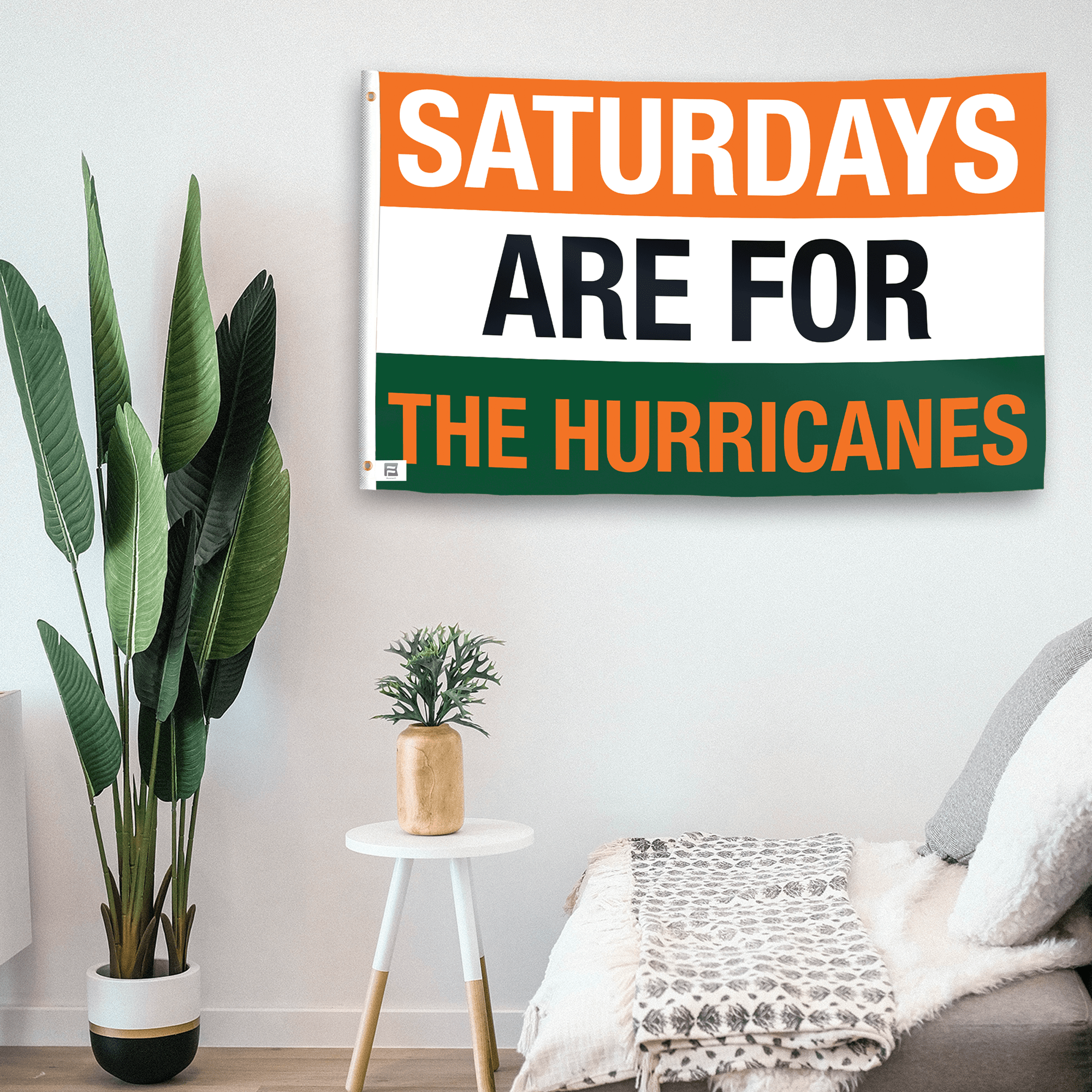 In a home setting, a flag with the saying "Saturdays Are for the Hurricanes" is mounted on a white wall by a side table.