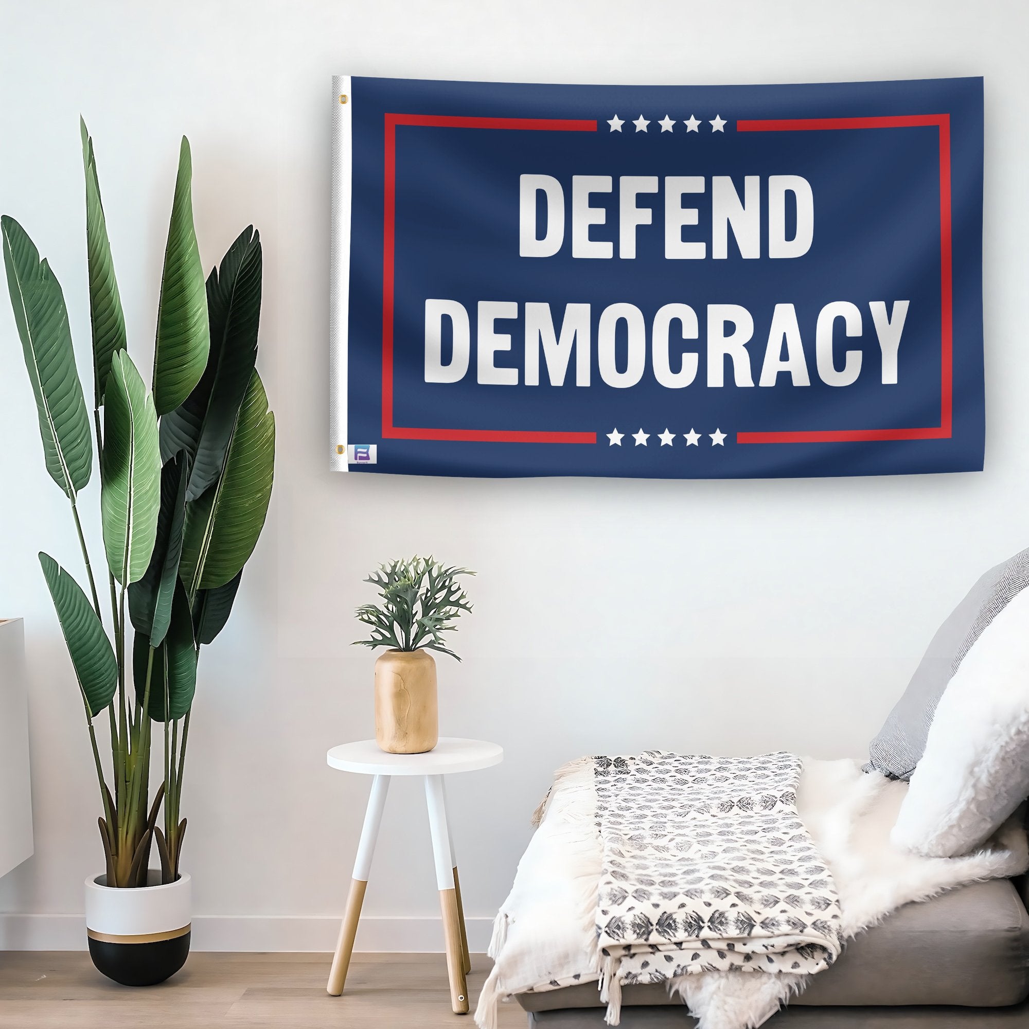 In a home setting, a flag with the saying "Defend Democracy Political" is mounted on a white wall by a side table.