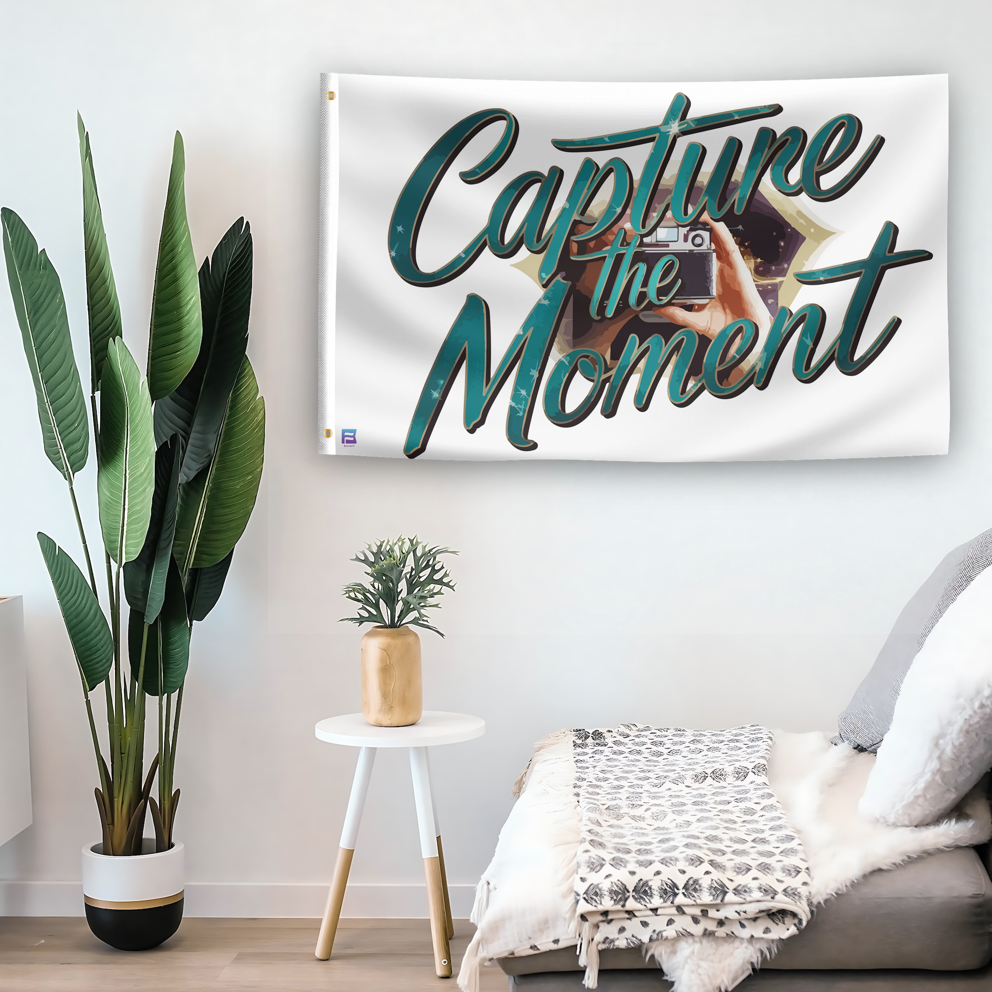 In a home setting, a flag with the saying "Capture The Moment Now" is mounted on a white wall by a side table.