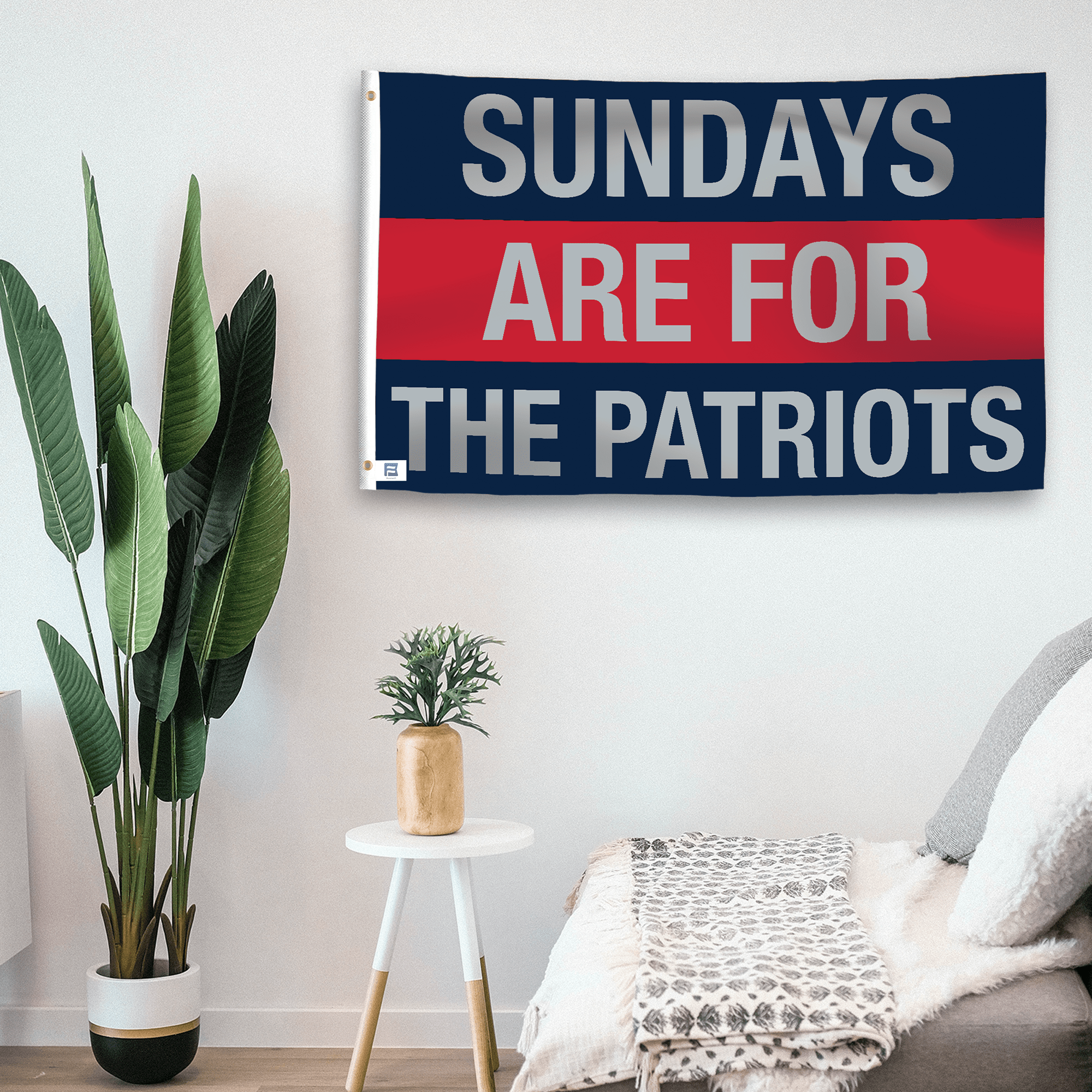 In a home setting, a flag with the saying "https://www.dropbox.com/scl/fi/f5c3rg7zsup72ckbwj76h/sundays-are-for-the-patriots_room.png?rlkey=cc3kumoaeu7uqrdx4h2mdfln8&raw=1" is mounted on a white wall by a side table.