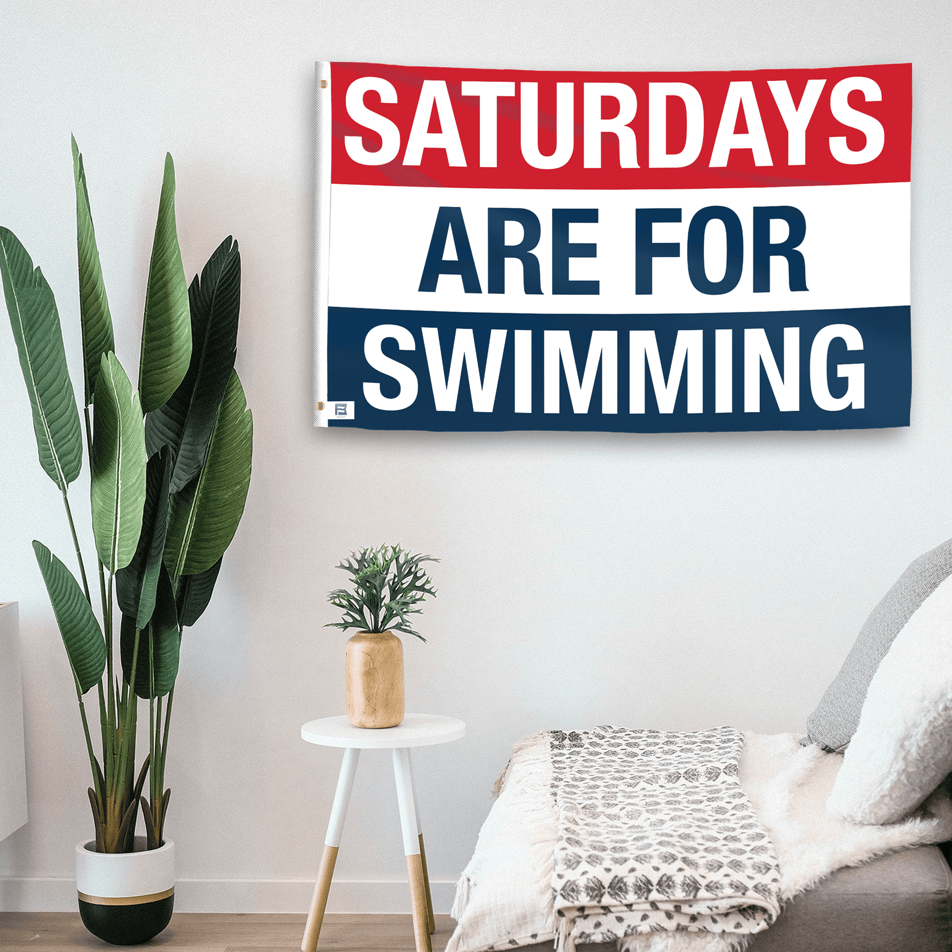 In a home setting, a flag with the saying "https://www.dropbox.com/scl/fi/pdpy6zx9l2ls3a2527cki/saturdays-are-for-swimming_room.png?rlkey=ato3fy6n8bo7cfm8ur61hb3yg&raw=1" is mounted on a white wall by a side table.