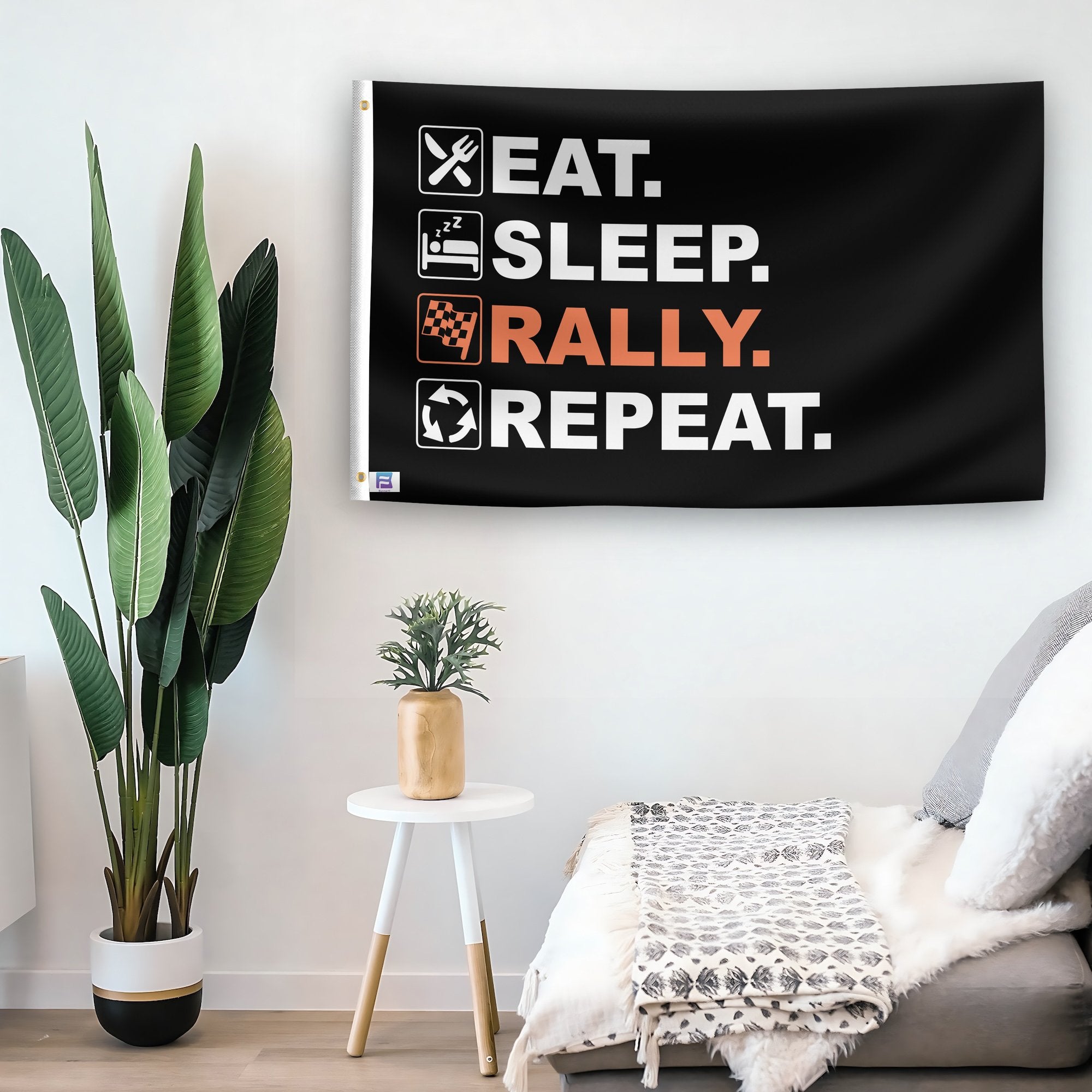 In a home setting, a flag with the saying "Eat Sleep Rally Repeat" is mounted on a white wall by a side table.