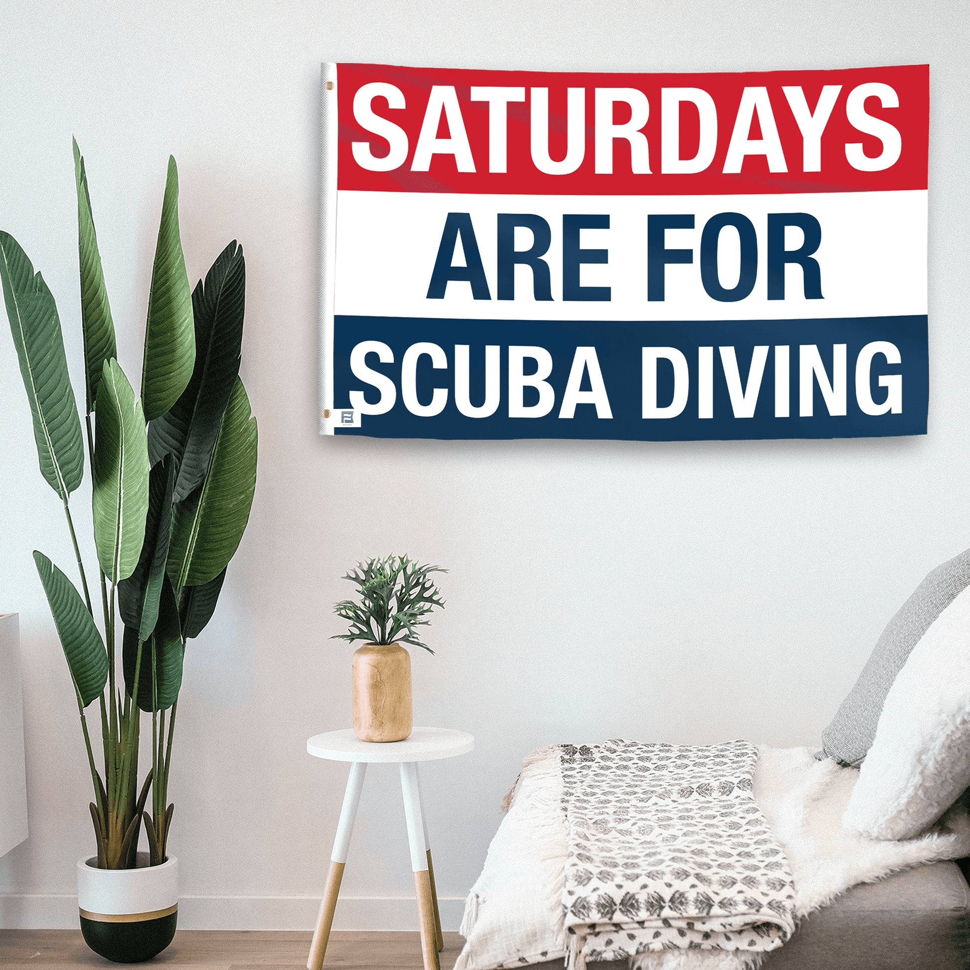 In a home setting, a flag with the saying "https://www.dropbox.com/scl/fi/z0ylxr885yb90j4aqmyvq/saturdays-are-for-scuba-diving_room.png?rlkey=uqrpijepbavjjtdmnqa85vst9&raw=1" is mounted on a white wall by a side table.