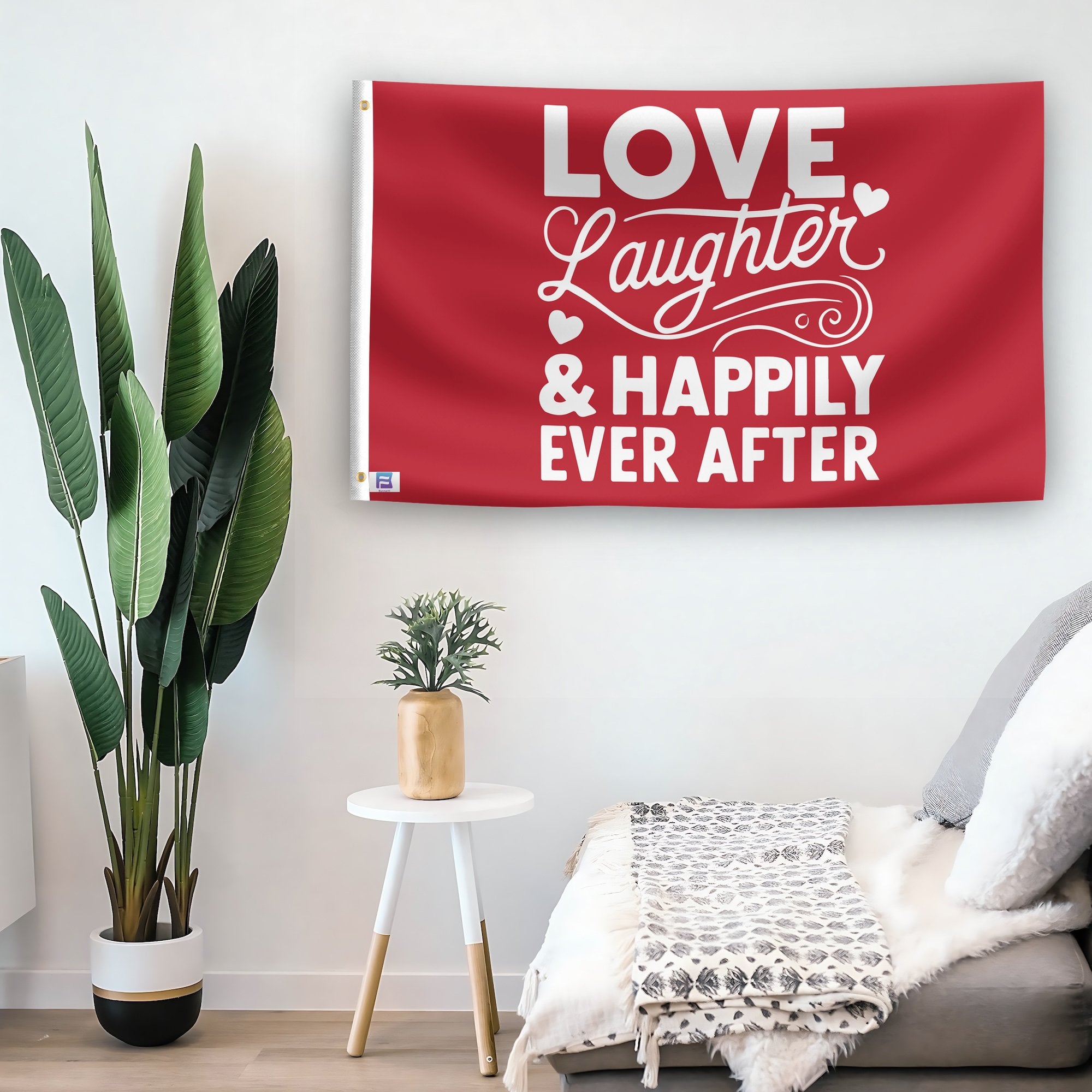 In a home setting, a flag with the saying "Love Laughter & Happily Ever After Wedding" is mounted on a white wall by a side table.