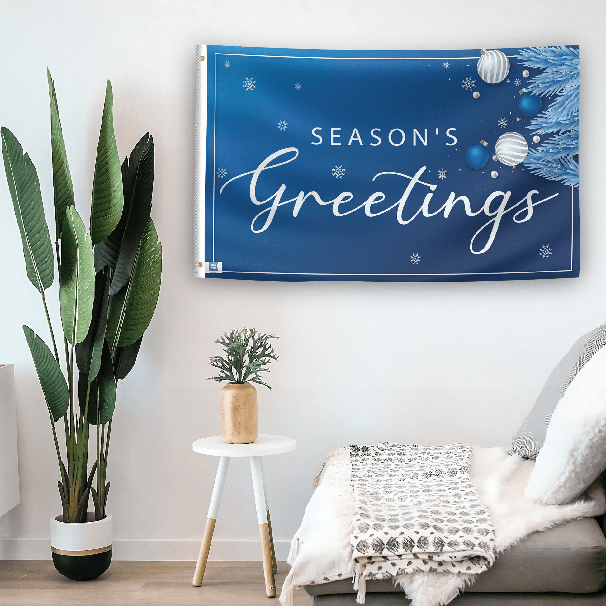 In a home setting, a flag with the saying "Season's Greetings" is mounted on a white wall by a side table.