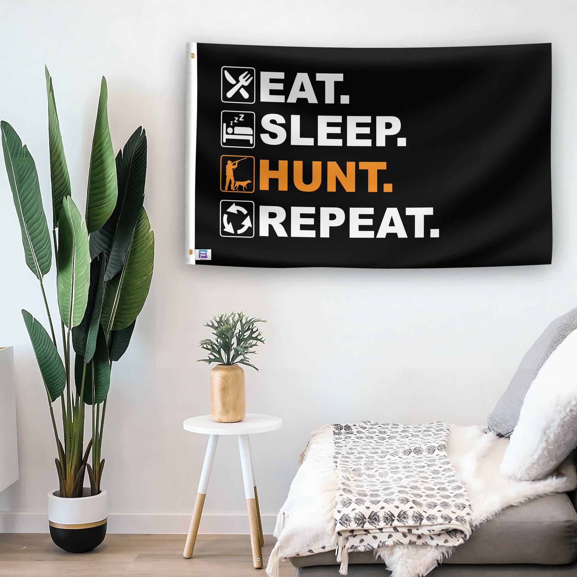 In a home setting, a flag with the saying "Eat Sleep Hunt Repeat" is mounted on a white wall by a side table.