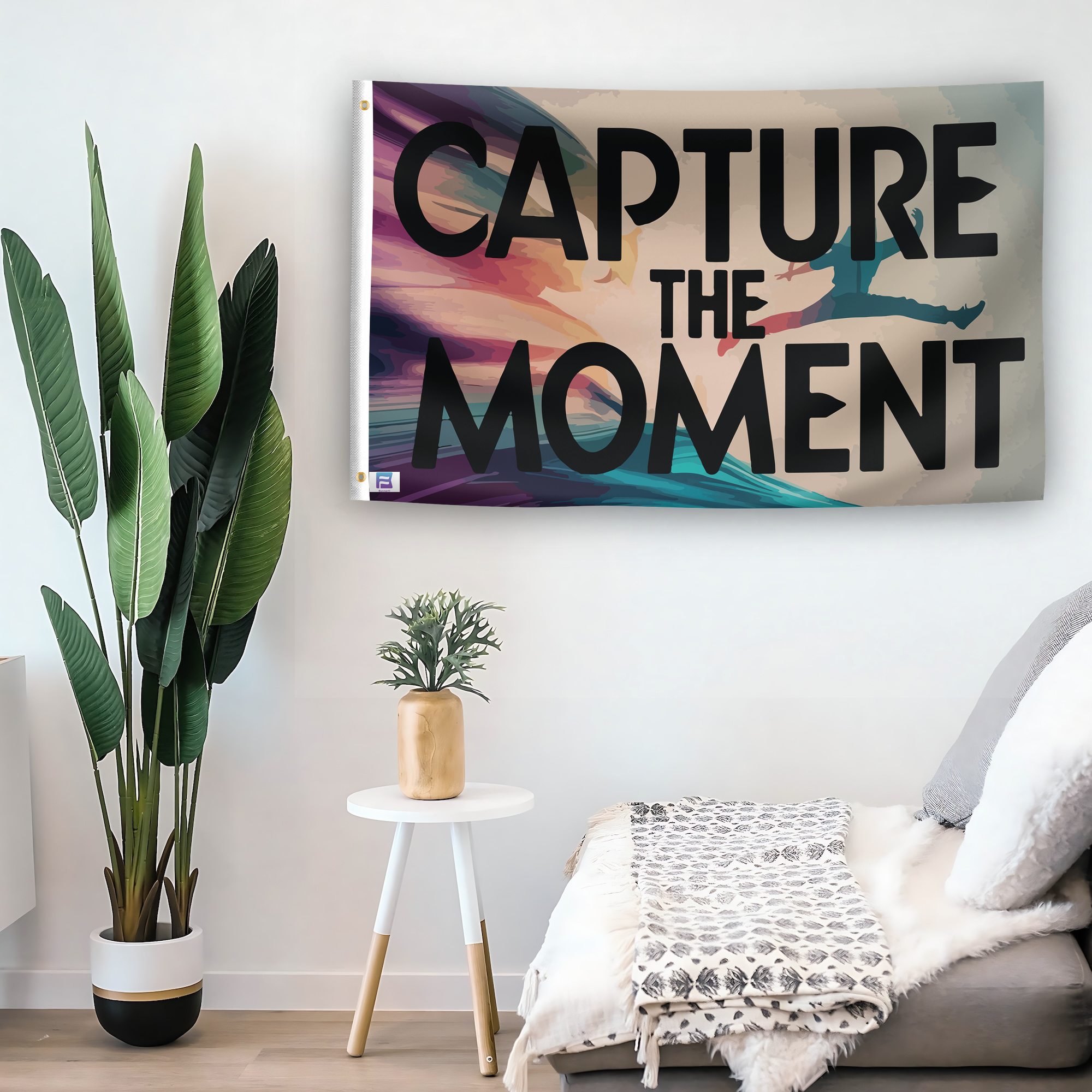 In a home setting, a flag with the saying "Capture The Moment" is mounted on a white wall by a side table.