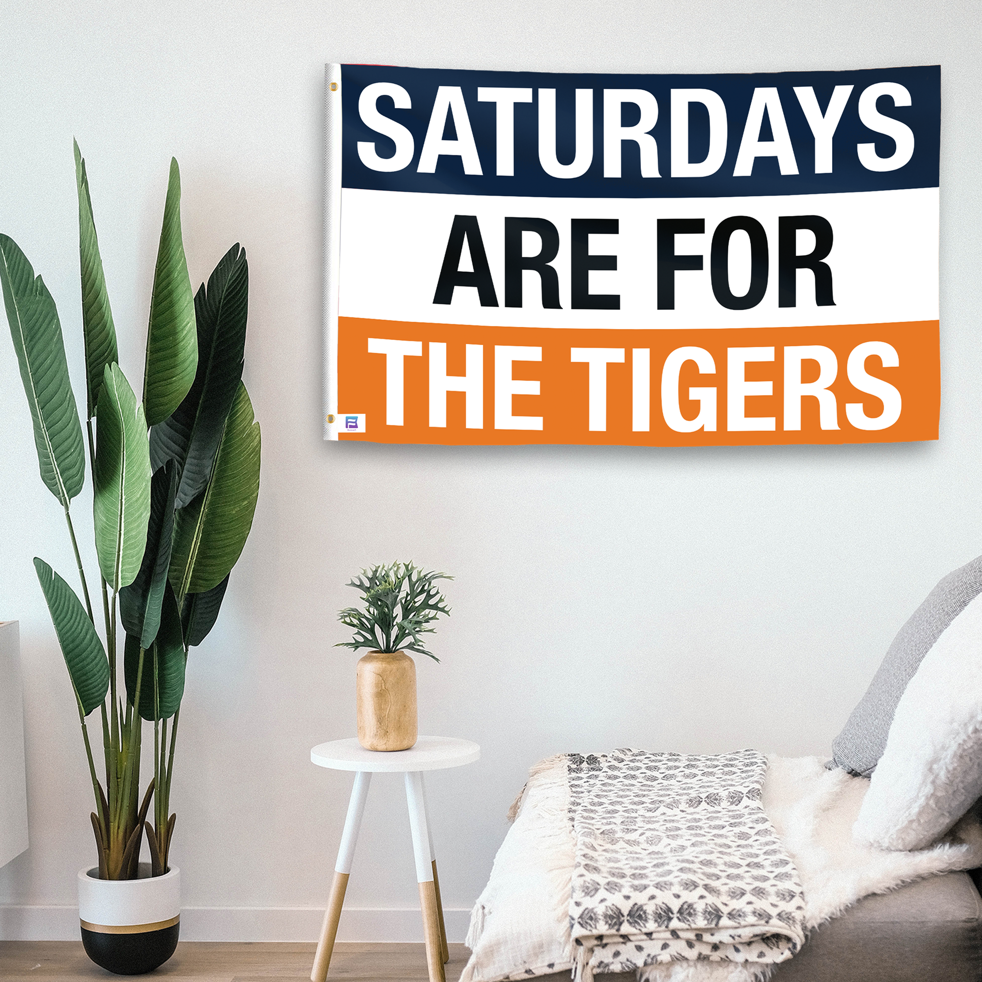 In a home setting, a flag with the saying "Saturdays Are for the Tigers Auburn" is mounted on a white wall by a side table.