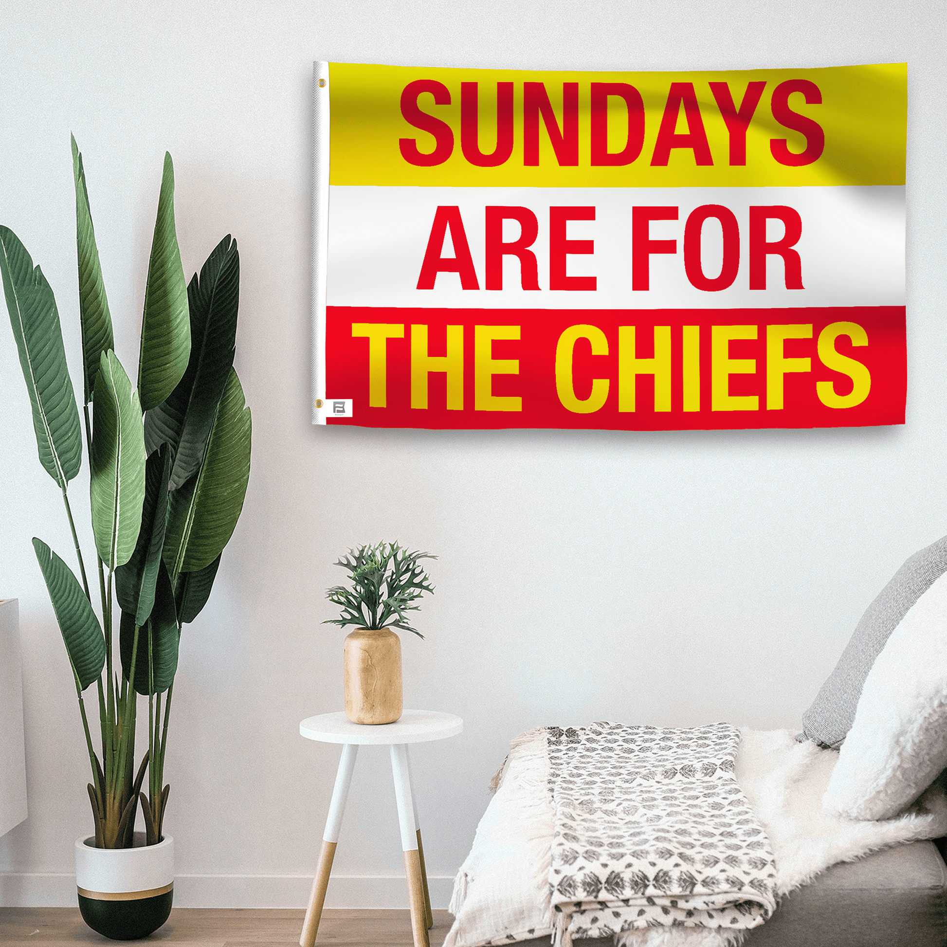 In a home setting, a flag with the saying "https://www.dropbox.com/scl/fi/ewh7vkrak7l0d3gldpnw2/sundays-are-for-the-chiefs_room.png?rlkey=4iykvsbzo8knju1q69jvyw7no&raw=1" is mounted on a white wall by a side table.