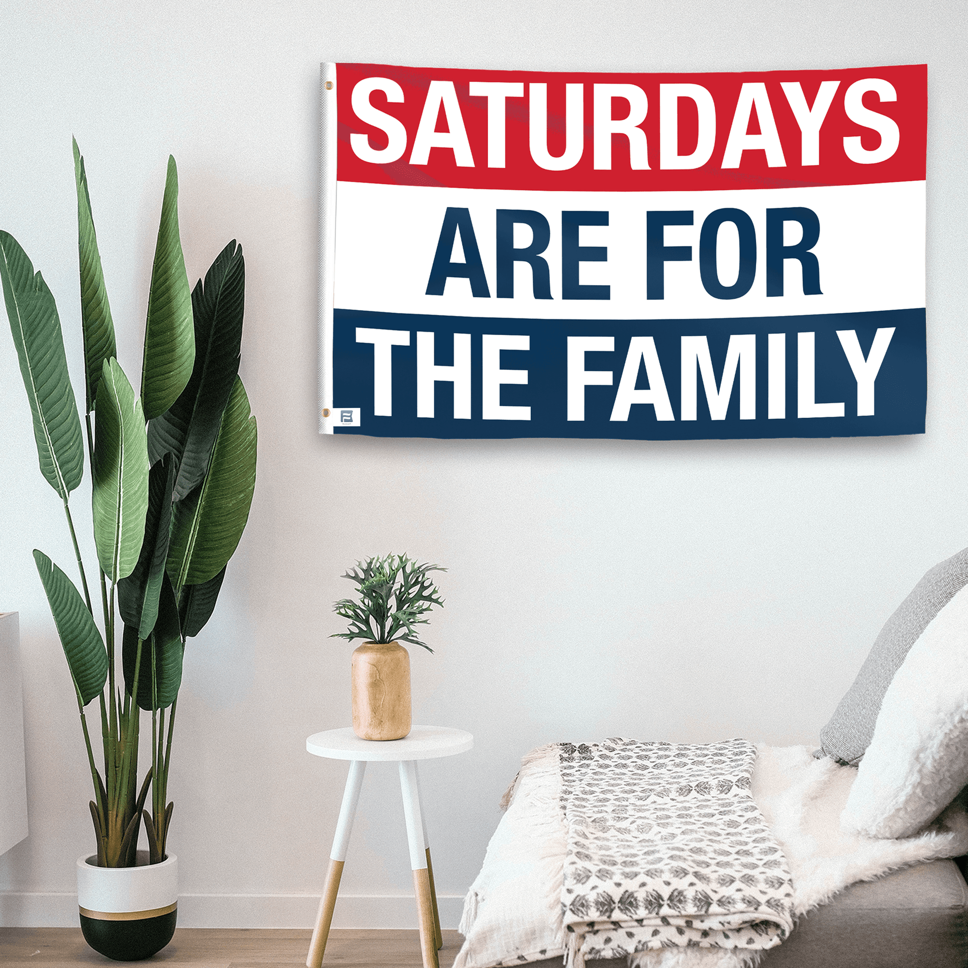 In a home setting, a flag with the saying "https://www.dropbox.com/scl/fi/b31qis4e57yxzotrdgx5l/saturdays-are-for-the-family_room.png?rlkey=l8m7wdff73htf5hdr2zdowwxd&raw=1" is mounted on a white wall by a side table.