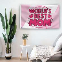 Load image into Gallery viewer, In a home setting, a flag with the saying &quot;World&#39;s Best Mom Gift&quot; is mounted on a white wall by a side table.
