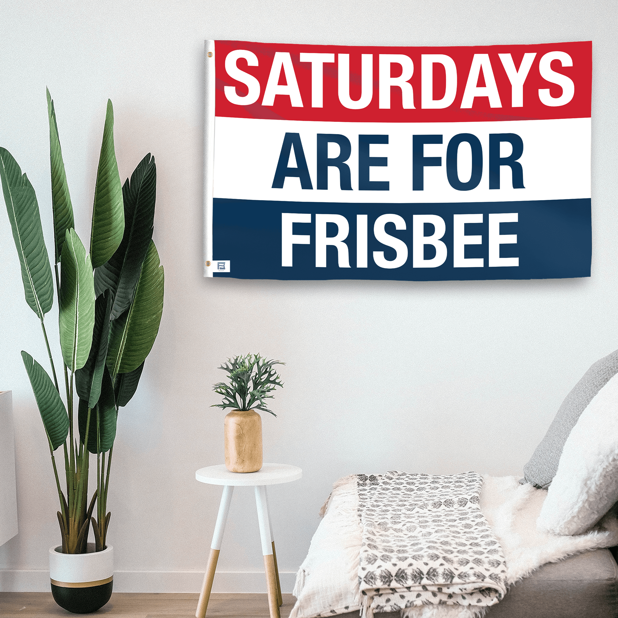 In a home setting, a flag with the saying "https://www.dropbox.com/scl/fi/37pr4ko1768dmqd7x8oeg/saturdays-are-for-frisbee_room.png?rlkey=u85k943hdr3iat8hmak2evhwx&raw=1" is mounted on a white wall by a side table.