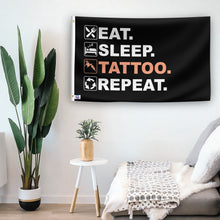 Load image into Gallery viewer, In a home setting, a flag with the saying &quot;Eat Sleep Tattoo Repeat&quot; is mounted on a white wall by a side table.
