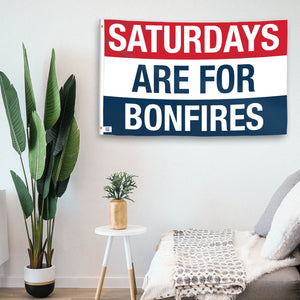 In a home setting, a flag with the saying "https://www.dropbox.com/scl/fi/t8oyrt9l1ah3jrv7ba7vo/saturdays-are-for-bonfires_room.png?rlkey=f4g8ehnhjqh1jppw9t9ot14c5&raw=1" is mounted on a white wall by a side table.