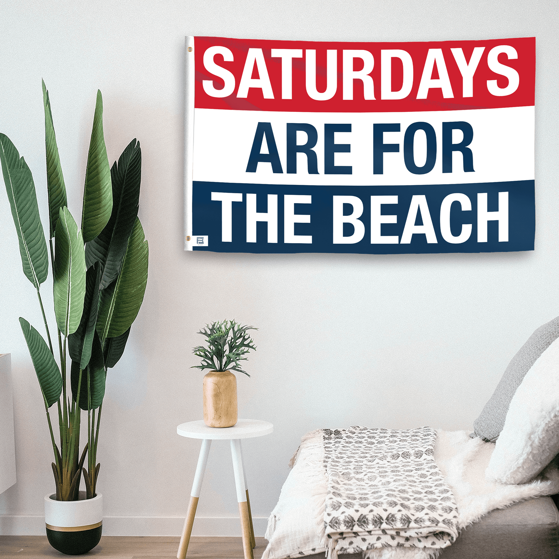 In a home setting, a flag with the saying "https://www.dropbox.com/scl/fi/8n65lo8bf25u191vojvs8/saturdays-are-for-the-beach_room.png?rlkey=2efedj9zw42w1vzyx4ip44fcr&raw=1" is mounted on a white wall by a side table.