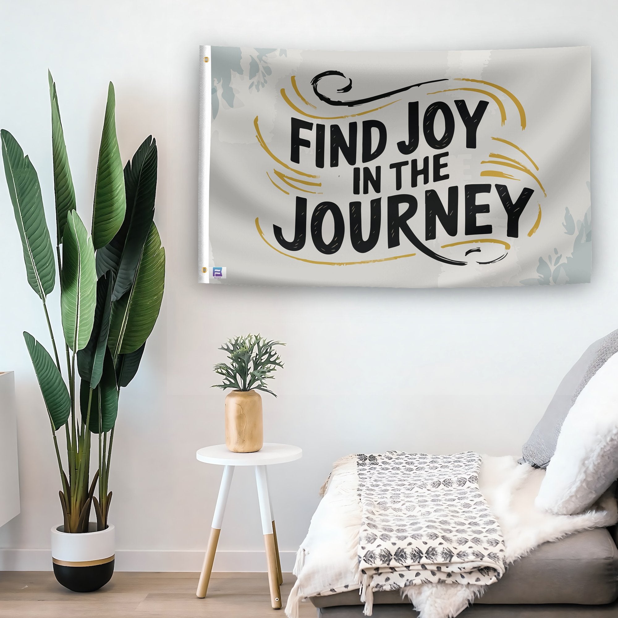 In a home setting, a flag with the saying "Find Joy In The Journey" is mounted on a white wall by a side table.