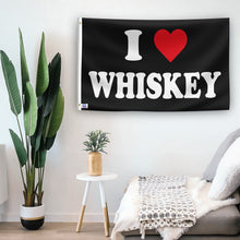 Load image into Gallery viewer, In a home setting, a flag with the saying &quot;I Love Whiskey&quot; is mounted on a white wall by a side table.
