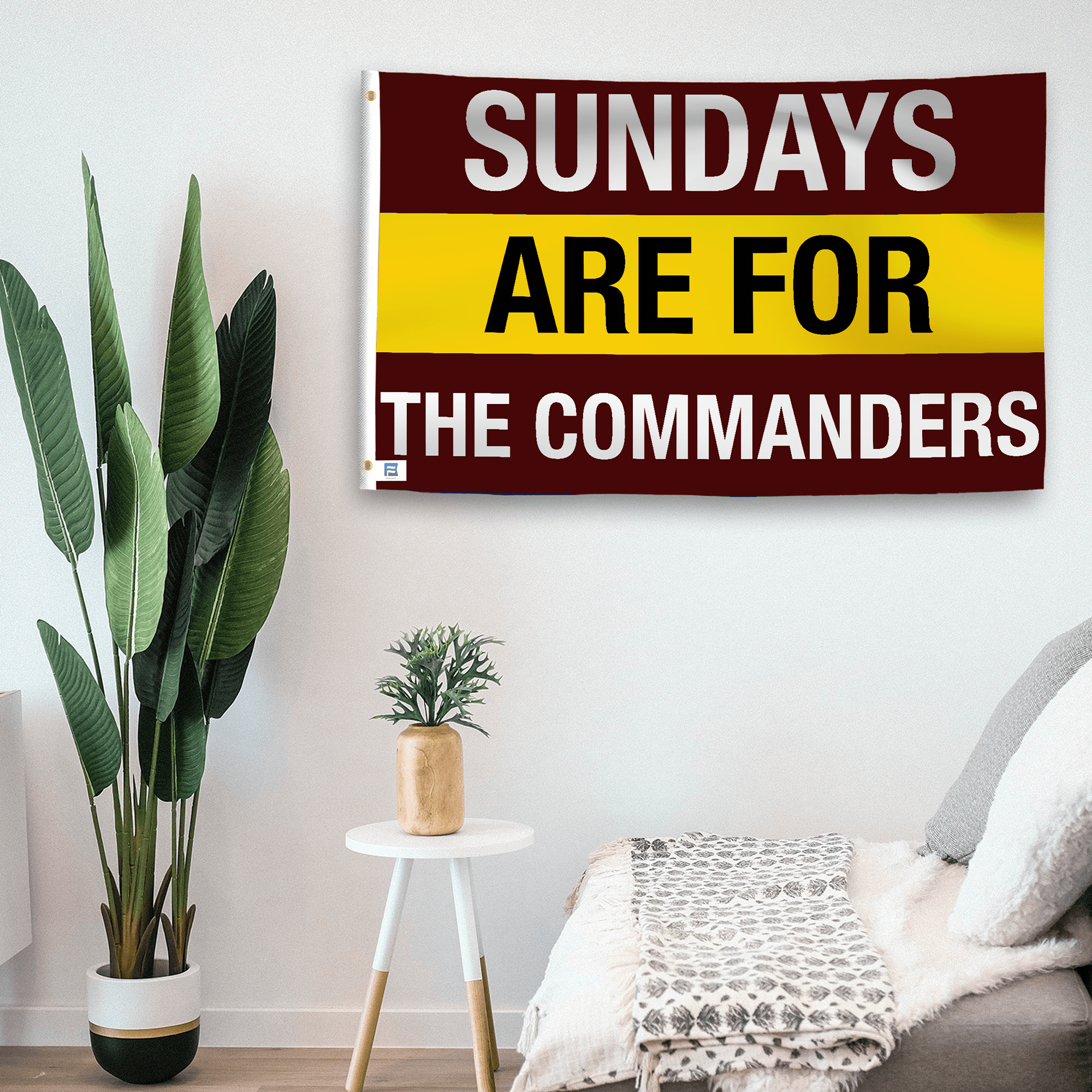 In a home setting, a flag with the saying "https://www.dropbox.com/scl/fi/sxewgtn6kw0irupcch6xf/sundays-are-for-the-commanders_room.png?rlkey=bni4hoir86t3c6k8w9bx1xj36&raw=1" is mounted on a white wall by a side table.