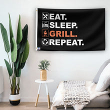 Load image into Gallery viewer, In a home setting, a flag with the saying &quot;Eat Sleep Grill Repeat&quot; is mounted on a white wall by a side table.
