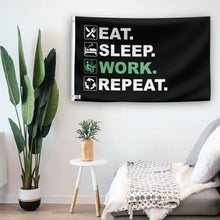 Load image into Gallery viewer, In a home setting, a flag with the saying &quot;Eat Sleep Work Repeat&quot; is mounted on a white wall by a side table.
