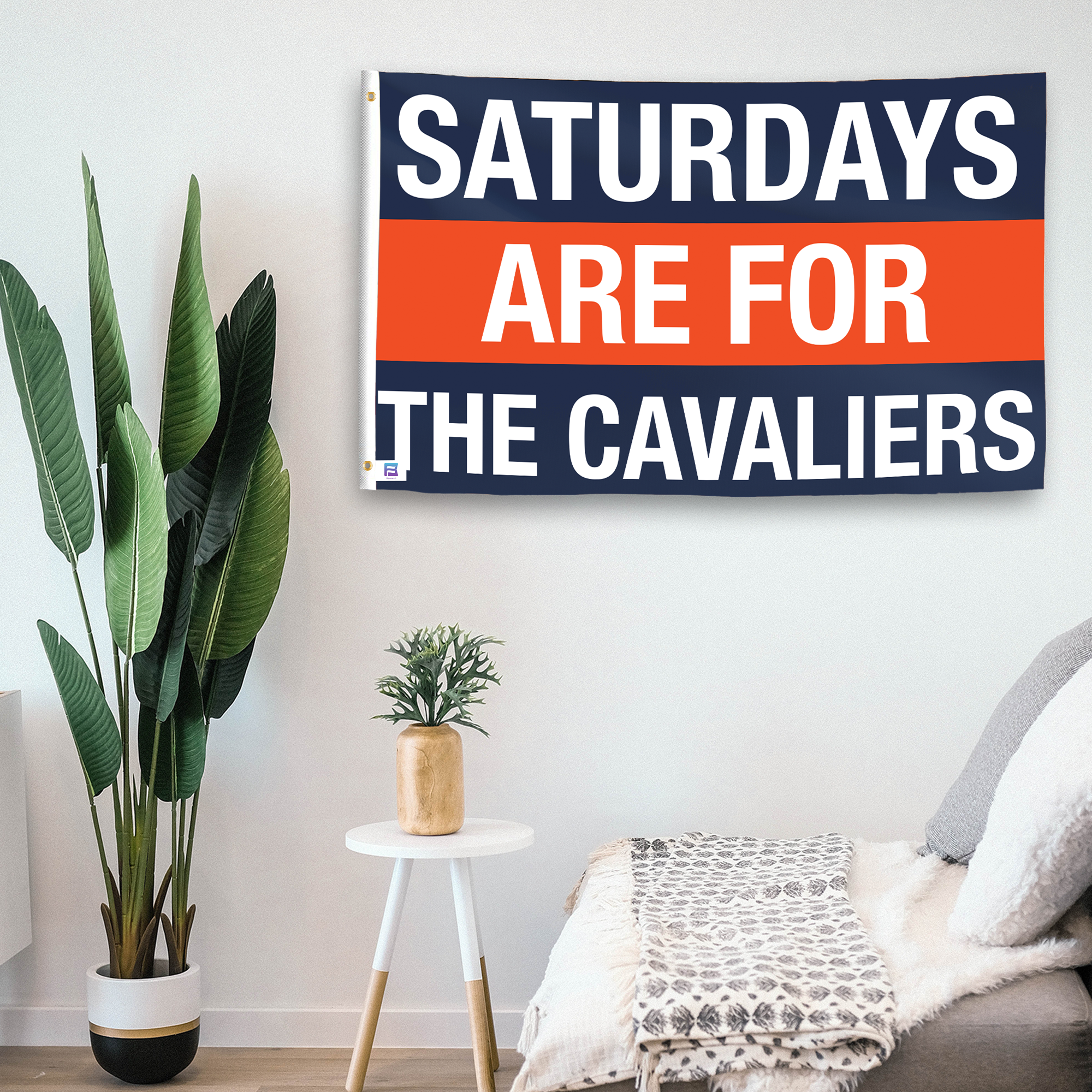 In a home setting, a flag with the saying "Saturdays Are for the Cavaliers" is mounted on a white wall by a side table.