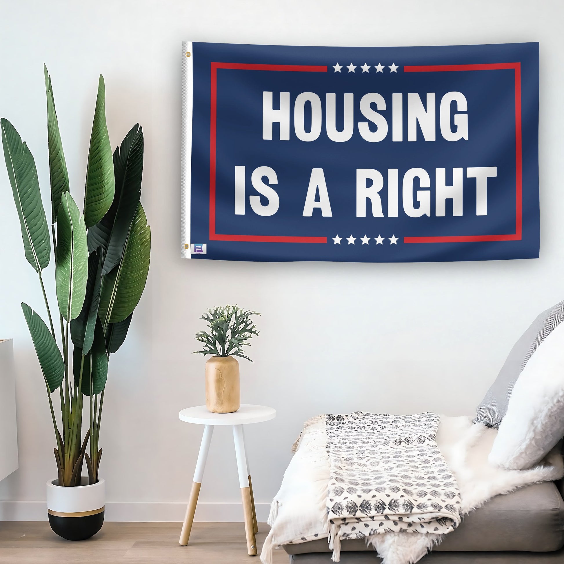 In a home setting, a flag with the saying "Housing Is A Right Political" is mounted on a white wall by a side table.