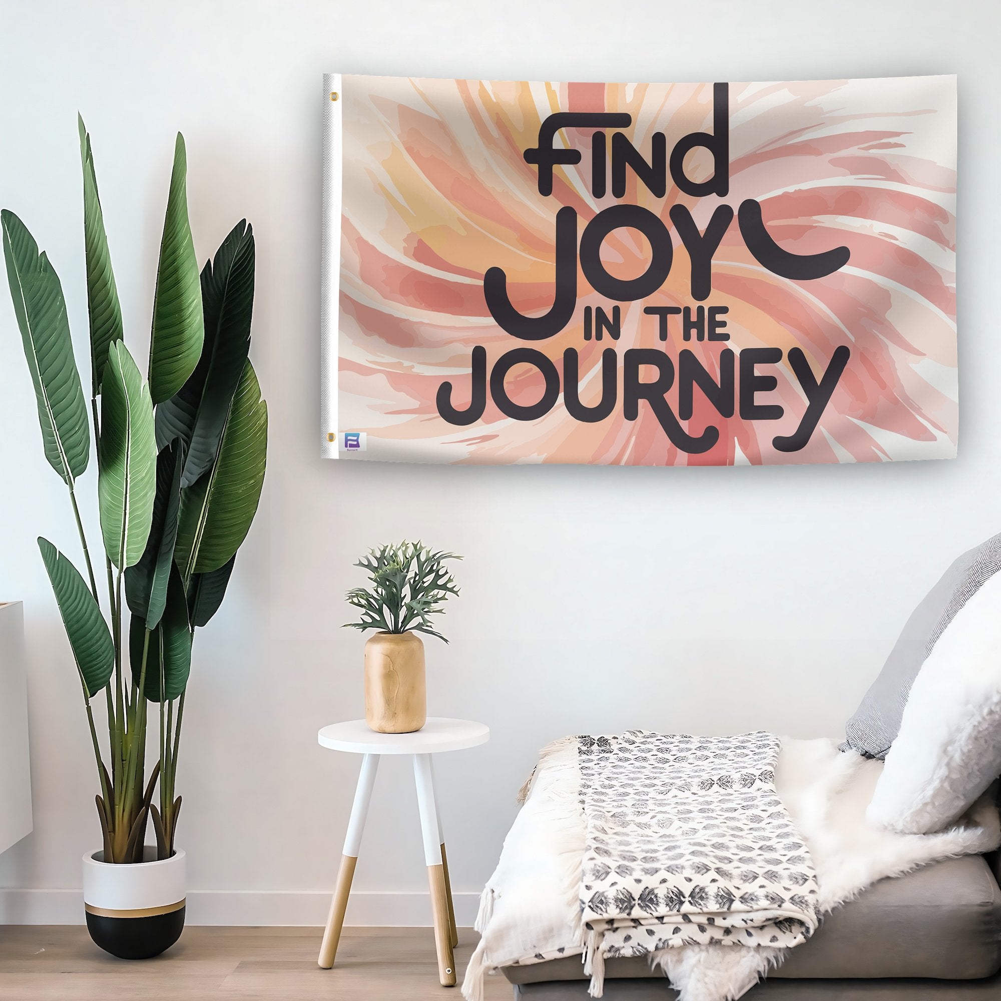 In a home setting, a flag with the saying "Find Joy In The Journey Motivational" is mounted on a white wall by a side table.