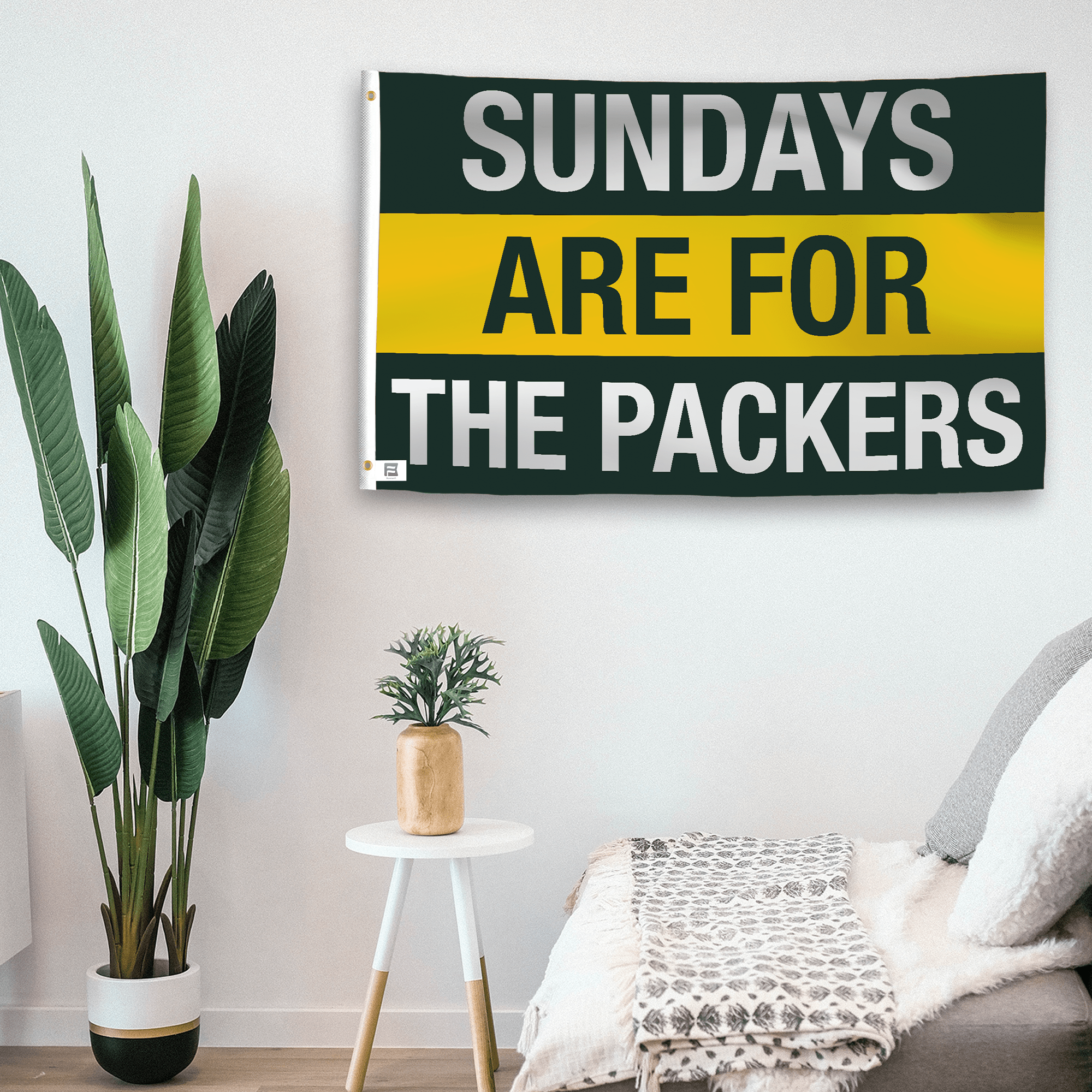 In a home setting, a flag with the saying "https://www.dropbox.com/scl/fi/hujf3k6k9p4cnxkf5lhxh/sundays-are-for-the-packers_room.png?rlkey=w4y4zt3xb7xgzflnurulktwh6&raw=1" is mounted on a white wall by a side table.