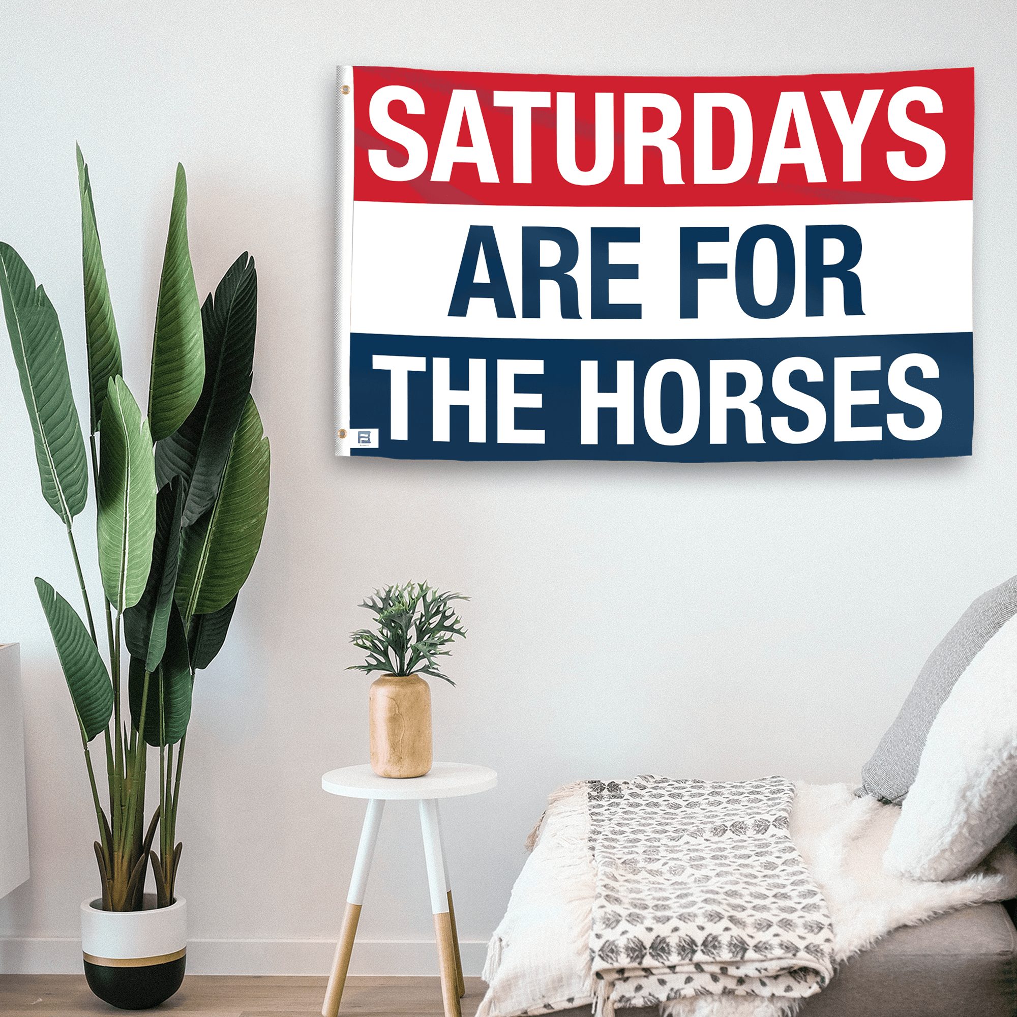 In a home setting, a flag with the saying "https://www.dropbox.com/scl/fi/s6cdamyt65lhdj6mupn89/saturdays-are-for-the-horses_room.png?rlkey=9bcpjlqz40l5s1ieux7922qk4&raw=1" is mounted on a white wall by a side table.