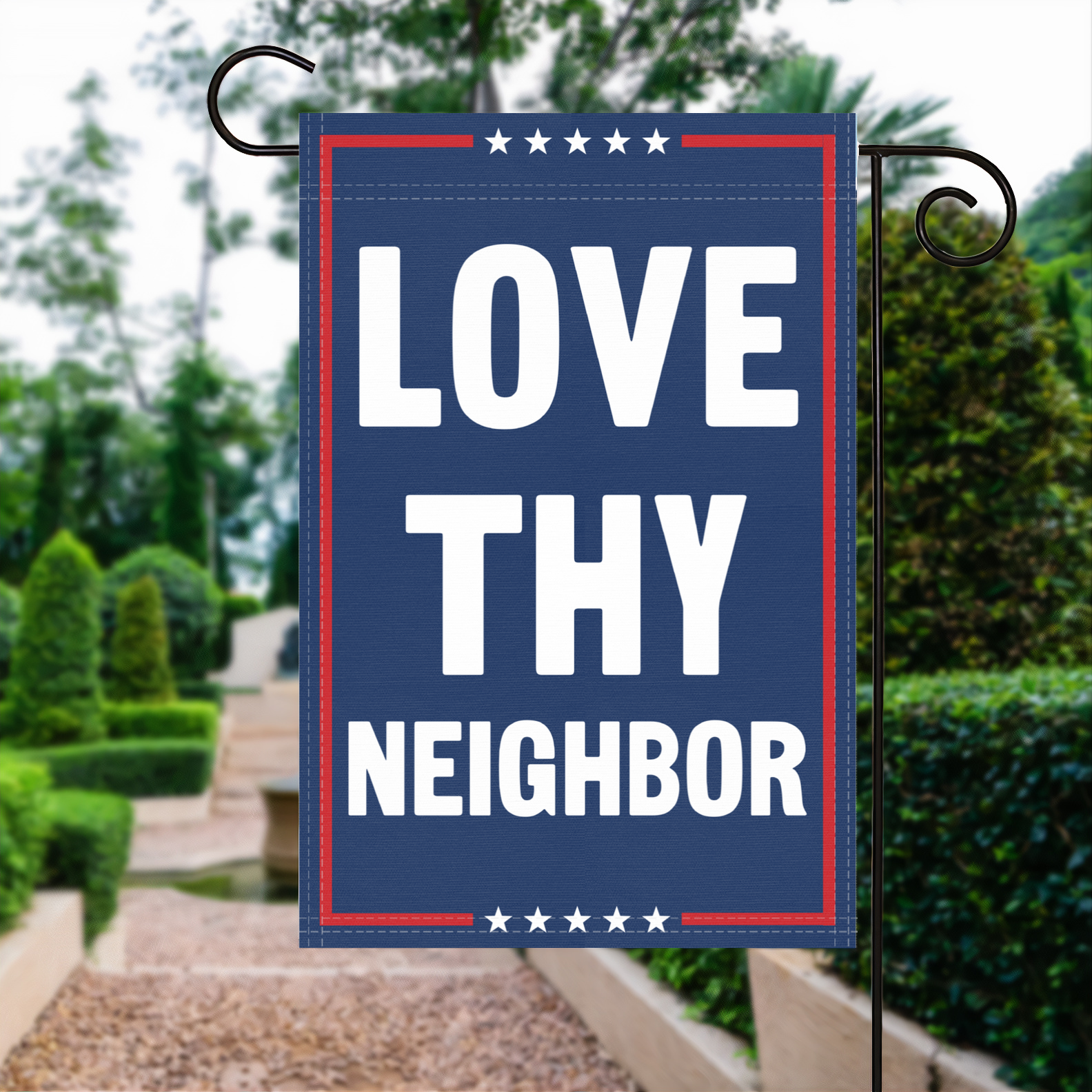 A red, white and blue political garden flag with the slogan Love Thy Neighbor.