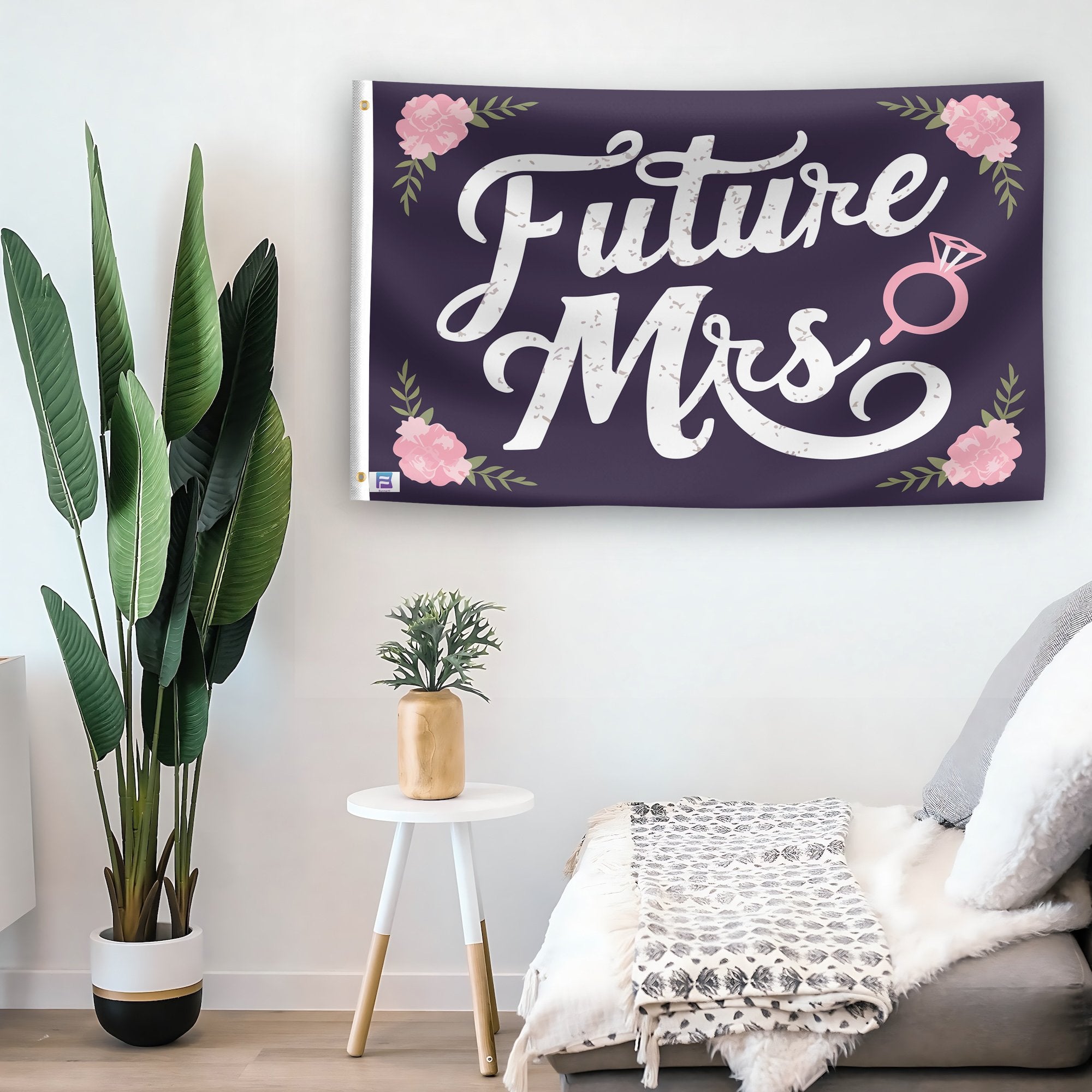 In a home setting, a flag with the saying "Future Mrs Engagement" is mounted on a white wall by a side table.