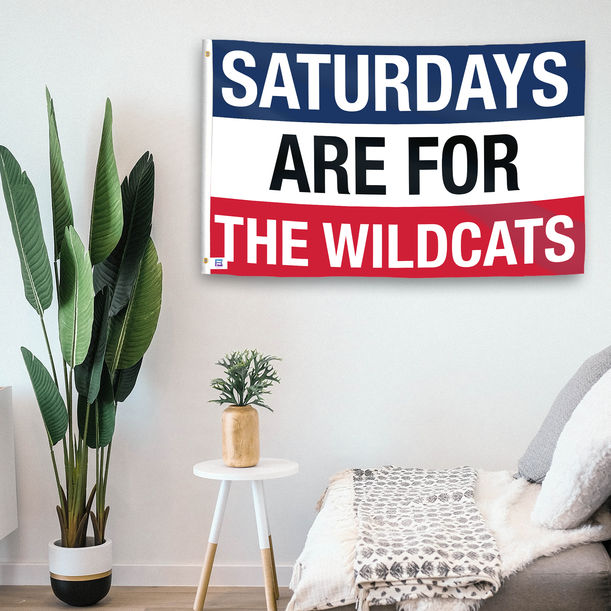 In a home setting, a flag with the saying "Saturdays Are for the Wildcats Arizona" is mounted on a white wall by a side table.