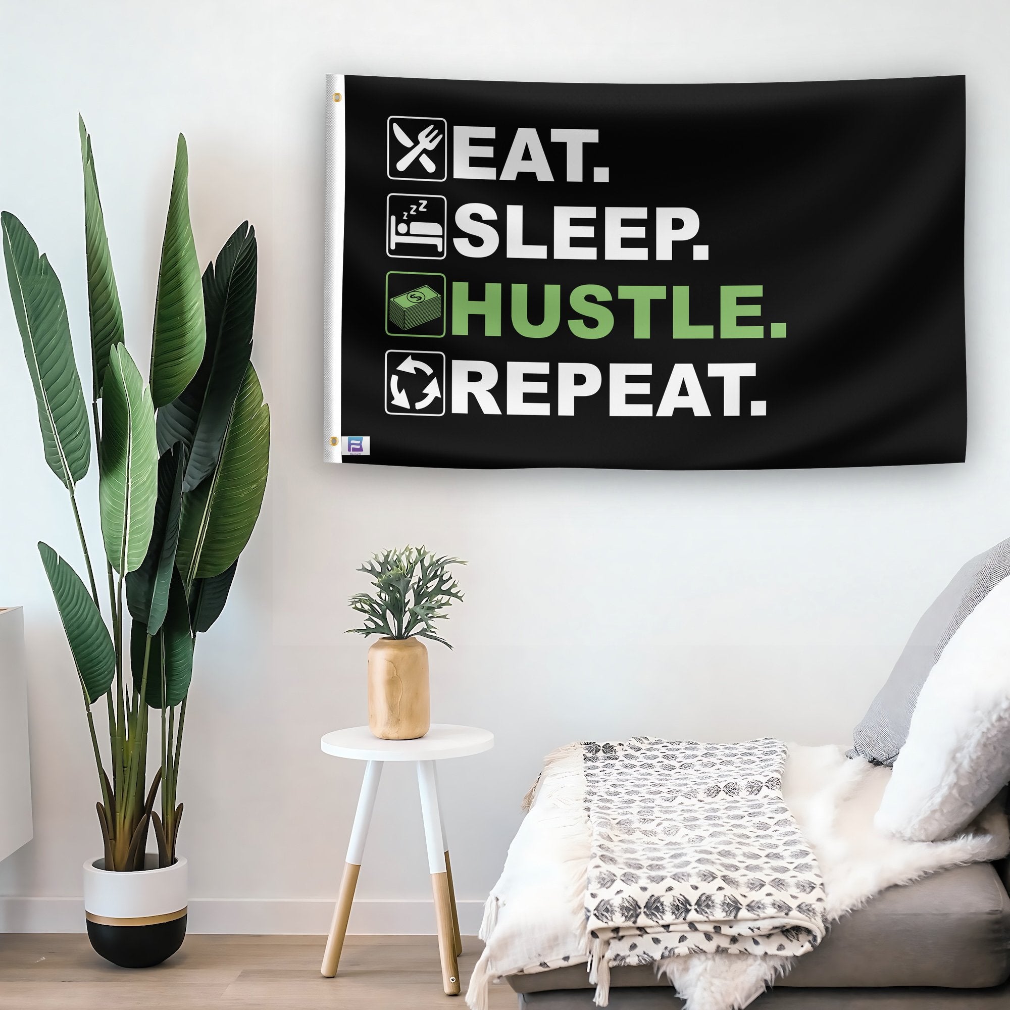 In a home setting, a flag with the saying "Eat Sleep Hustle Repeat" is mounted on a white wall by a side table.