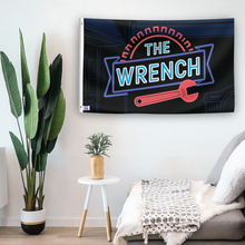 Load image into Gallery viewer, In a home setting, a flag with the saying &quot;The Wrench&quot; is mounted on a white wall by a side table.
