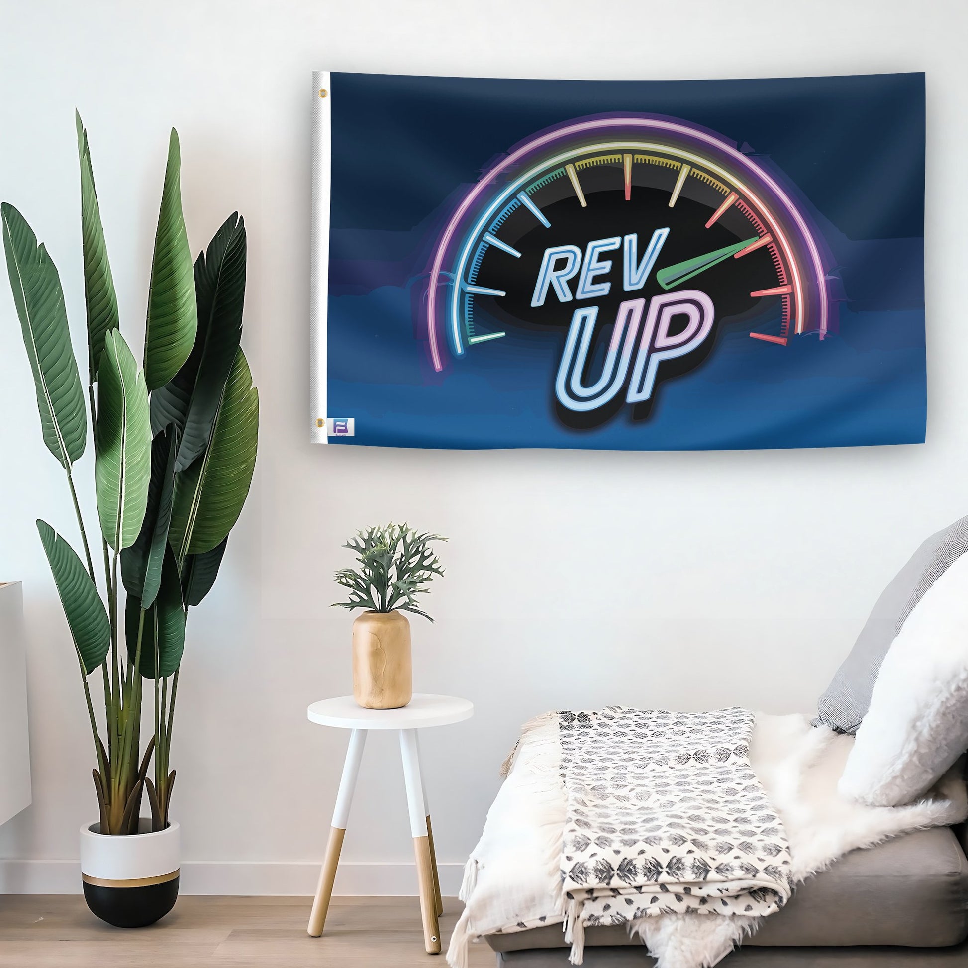 In a home setting, a flag with the saying "Rev Up" is mounted on a white wall by a side table.