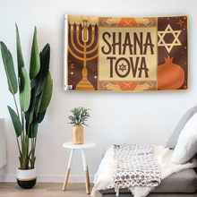 Load image into Gallery viewer, In a home setting, a flag with the saying &quot;Shana Tova&quot; is mounted on a white wall by a side table.
