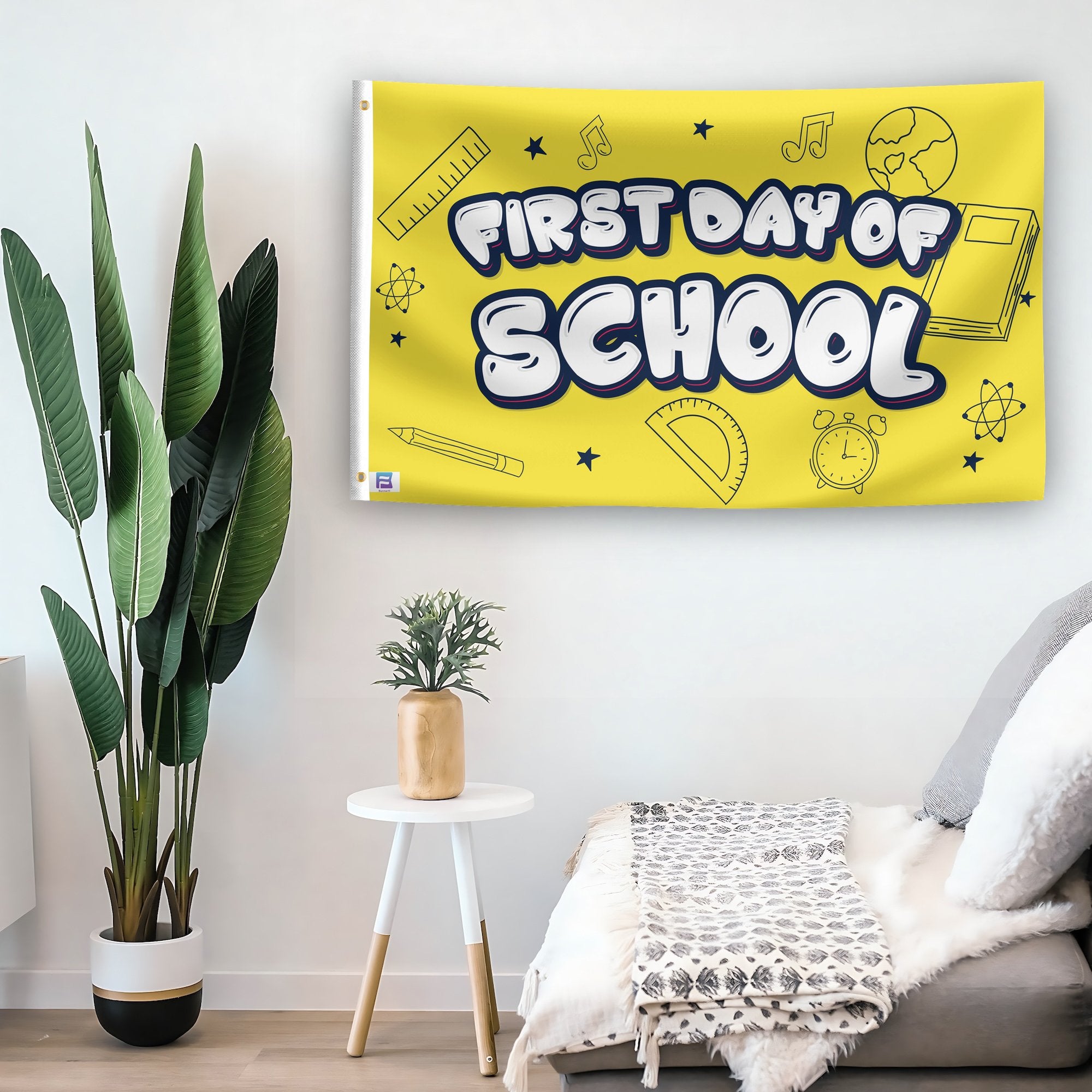 In a home setting, a flag with the saying "First Day Of School" is mounted on a white wall by a side table.