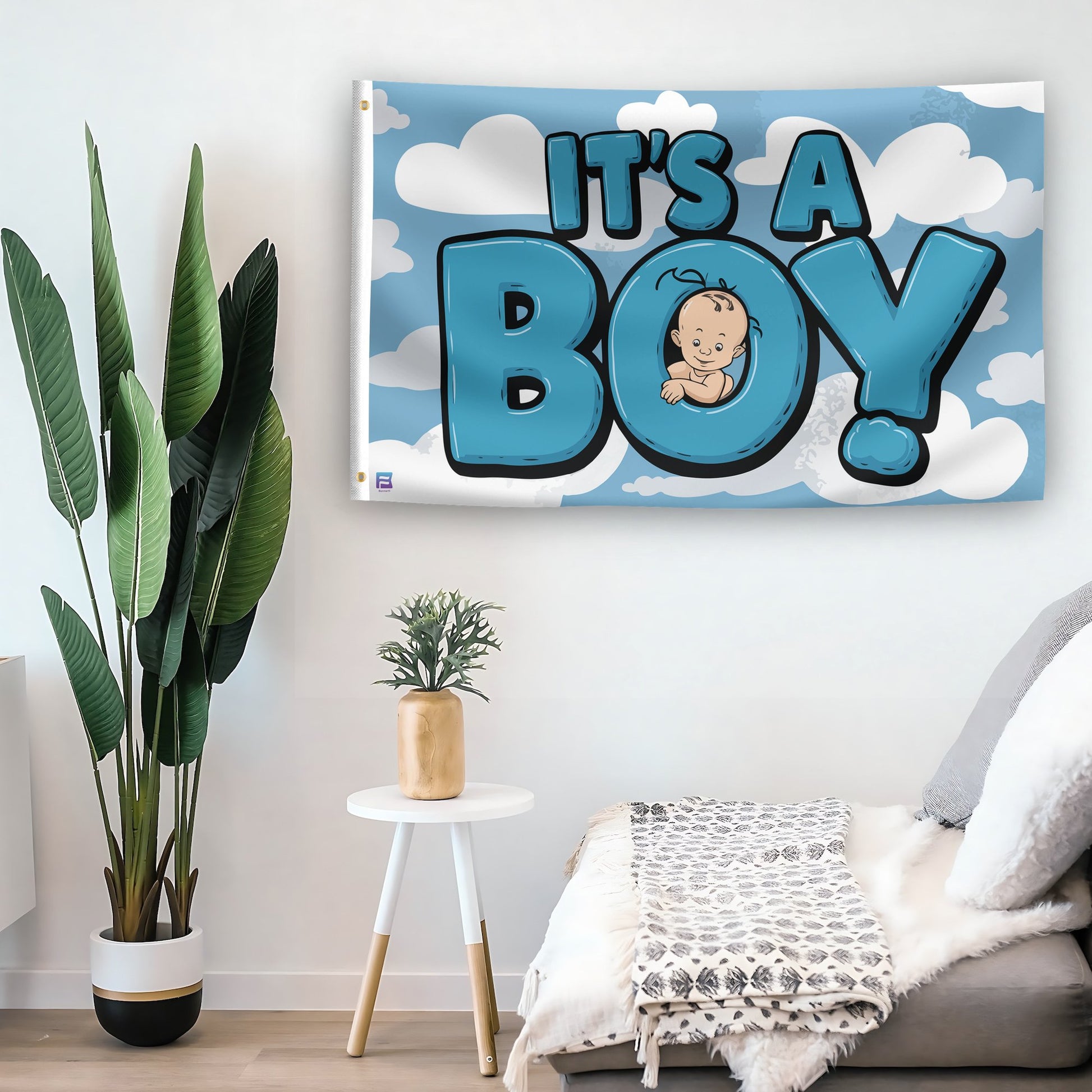 In a home setting, a flag with the saying "It's A Boy" is mounted on a white wall by a side table.