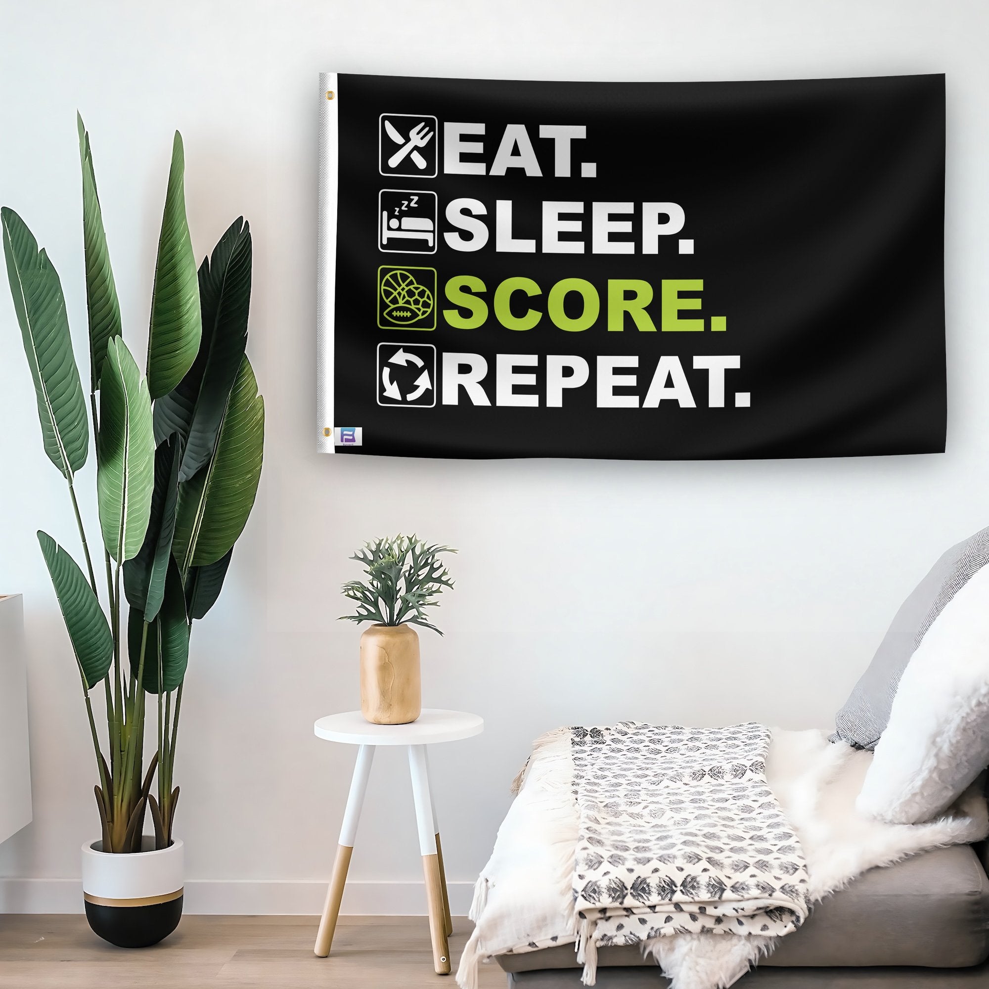 In a home setting, a flag with the saying "Eat Sleep Score Repeat" is mounted on a white wall by a side table.