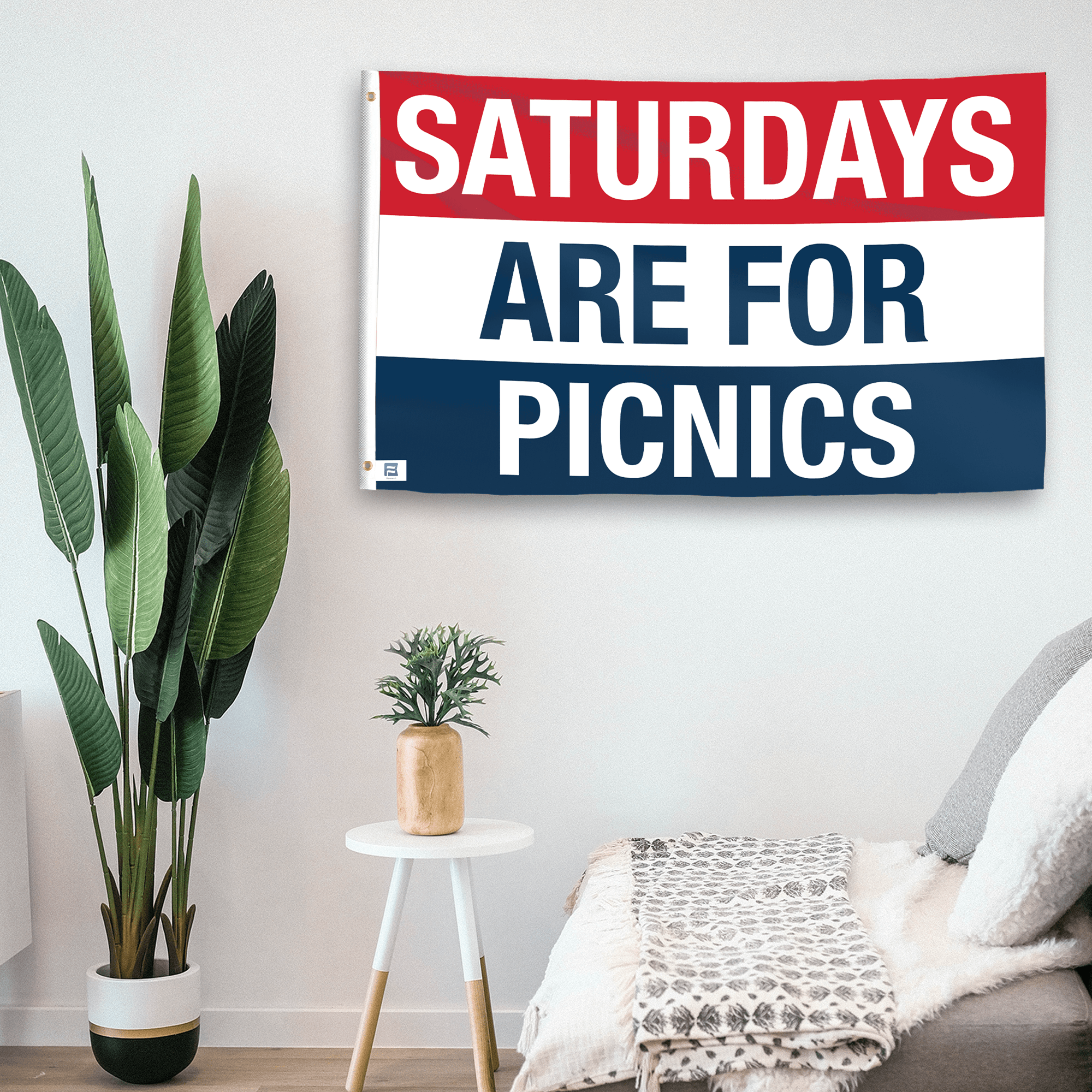 In a home setting, a flag with the saying "https://www.dropbox.com/scl/fi/gy4bltctbse1i9ldr80g6/saturdays-are-for-picnics_room.png?rlkey=2yzce87f83gamolerqc35m7sj&raw=1" is mounted on a white wall by a side table.