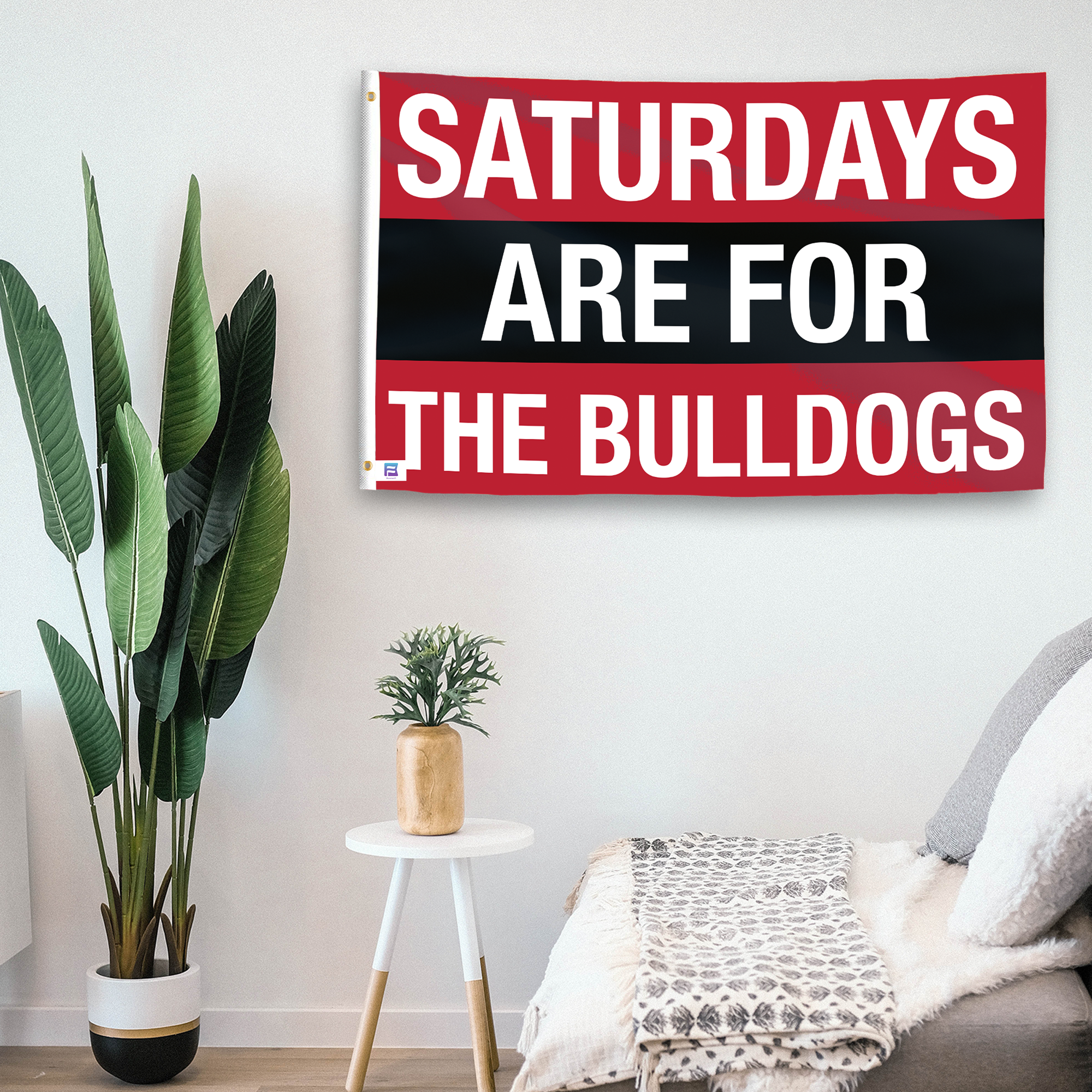 In a home setting, a flag with the saying "Saturdays Are for the Bulldogs Georgia" is mounted on a white wall by a side table.