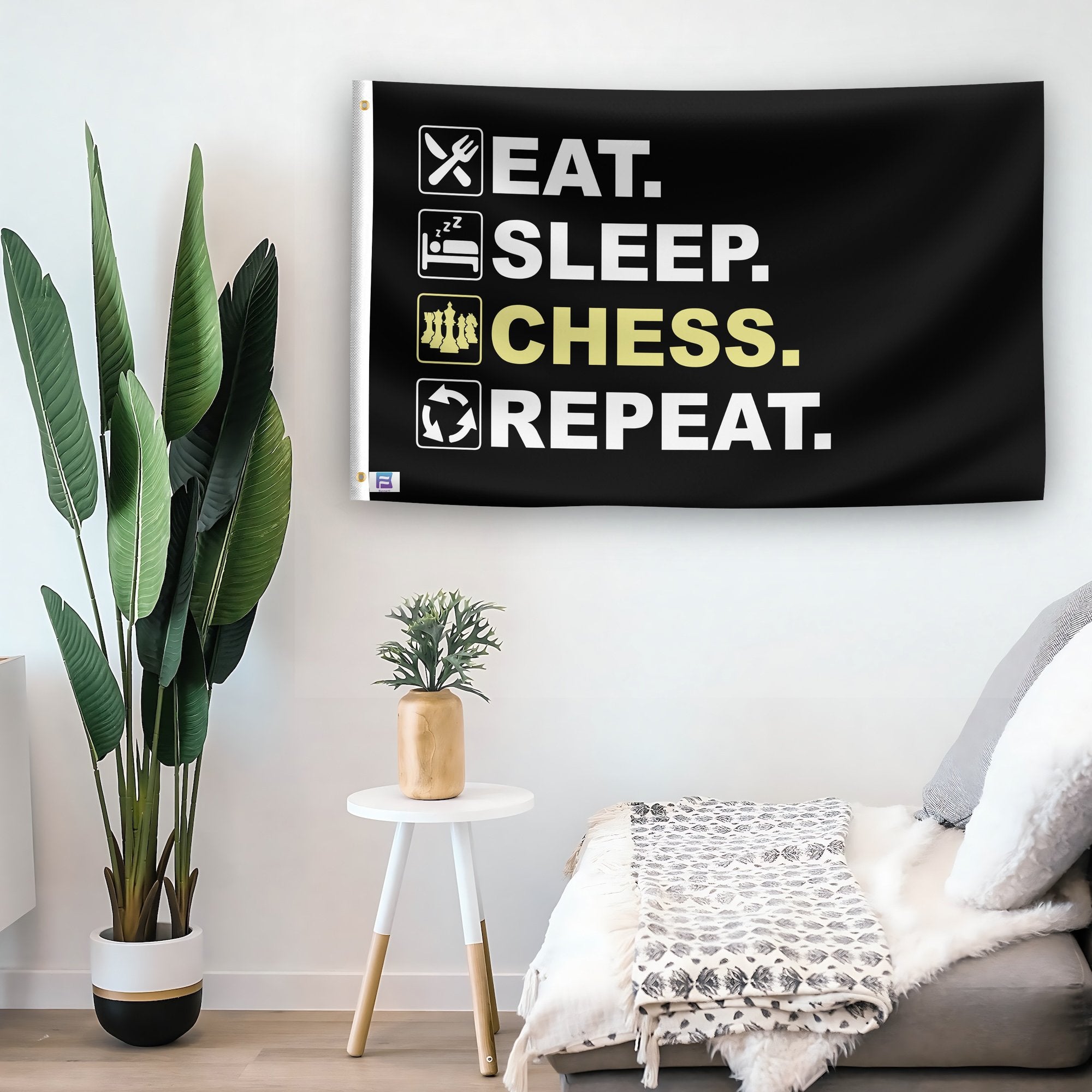 In a home setting, a flag with the saying "Eat Sleep Chess Repeat" is mounted on a white wall by a side table.