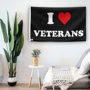 In a home setting, a flag with the saying "I Love Veterans" is mounted on a white wall by a side table.