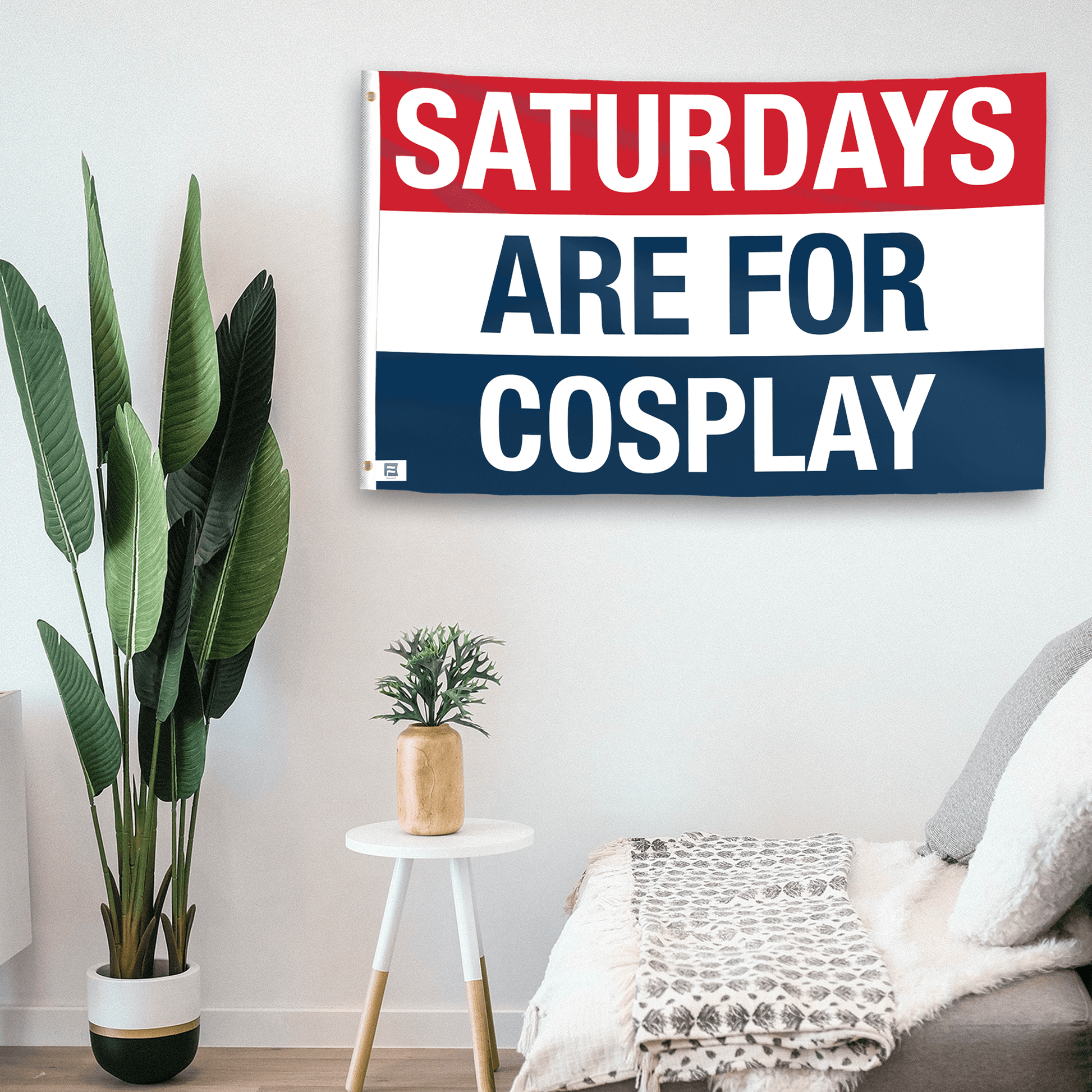 In a home setting, a flag with the saying "https://www.dropbox.com/scl/fi/ag4c9h5113sp0w2nmzsx8/saturdays-are-for-cosplay_room.png?rlkey=0w2m2zsgyuam3l68tww5cwxxn&raw=1" is mounted on a white wall by a side table.