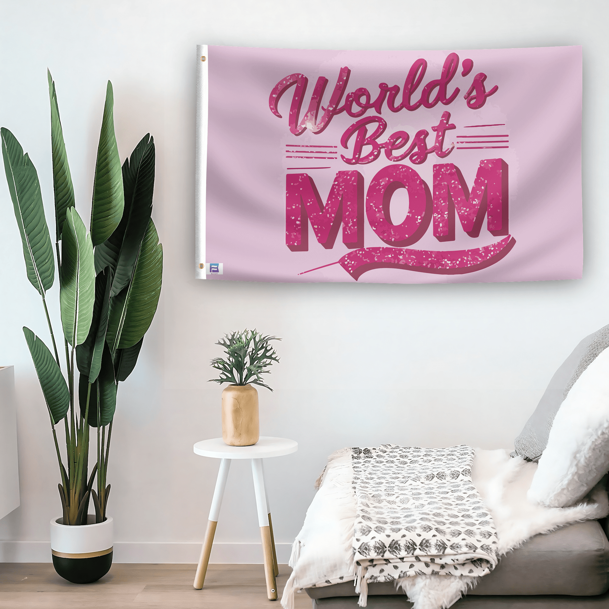 In a home setting, a flag with the saying "World's Best Mom" is mounted on a white wall by a side table.