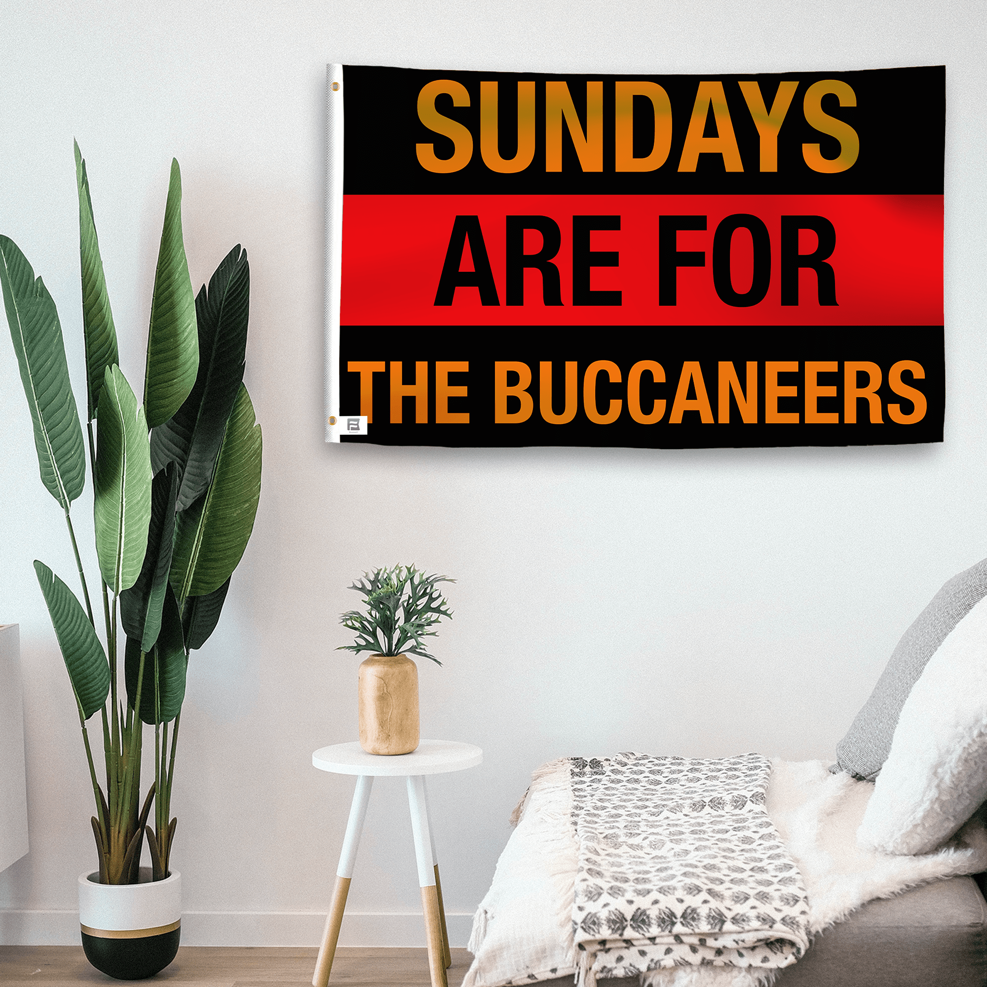 In a home setting, a flag with the saying "https://www.dropbox.com/scl/fi/gk30cvkni3xjb35ab2qgo/sundays-are-for-the-buccaneers_room.png?rlkey=evszj4xe5kigge98t40mr0h6t&raw=1" is mounted on a white wall by a side table.