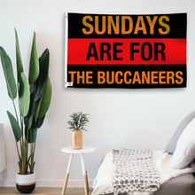 Load image into Gallery viewer, In a home setting, a flag with the saying &quot;https://www.dropbox.com/scl/fi/gk30cvkni3xjb35ab2qgo/sundays-are-for-the-buccaneers_room.png?rlkey=evszj4xe5kigge98t40mr0h6t&amp;raw=1&quot; is mounted on a white wall by a side table.
