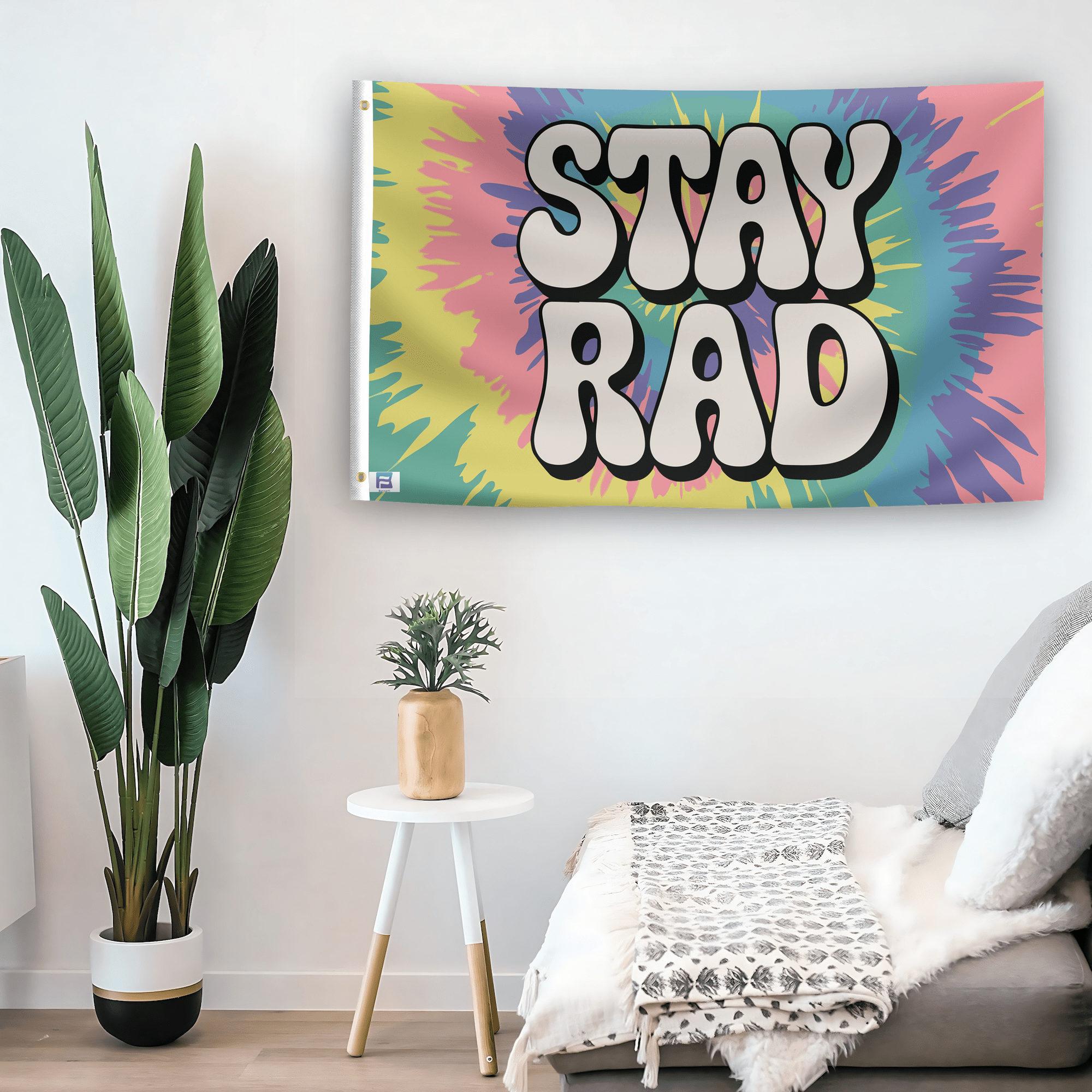 In a home setting, a flag with the saying "Stay Rad" is mounted on a white wall by a side table.