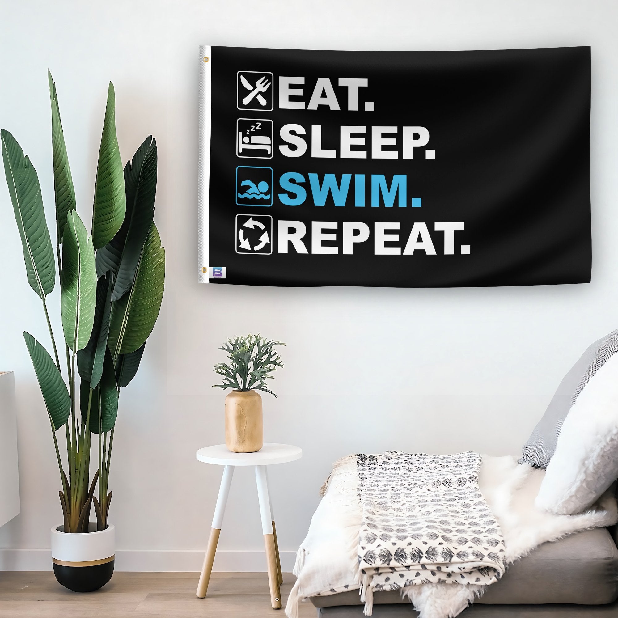 In a home setting, a flag with the saying "Eat Sleep Swim Repeat" is mounted on a white wall by a side table.